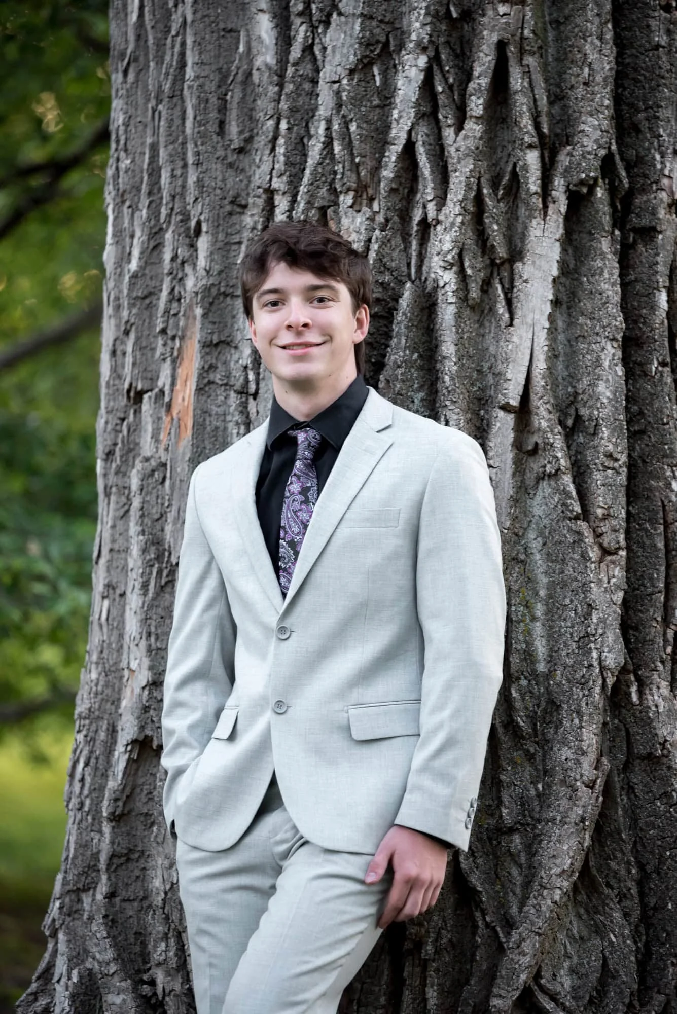 Senior guy leaning against a massive, textured tree trunk for a formal portrait taken by a St. Louis senior photographer.