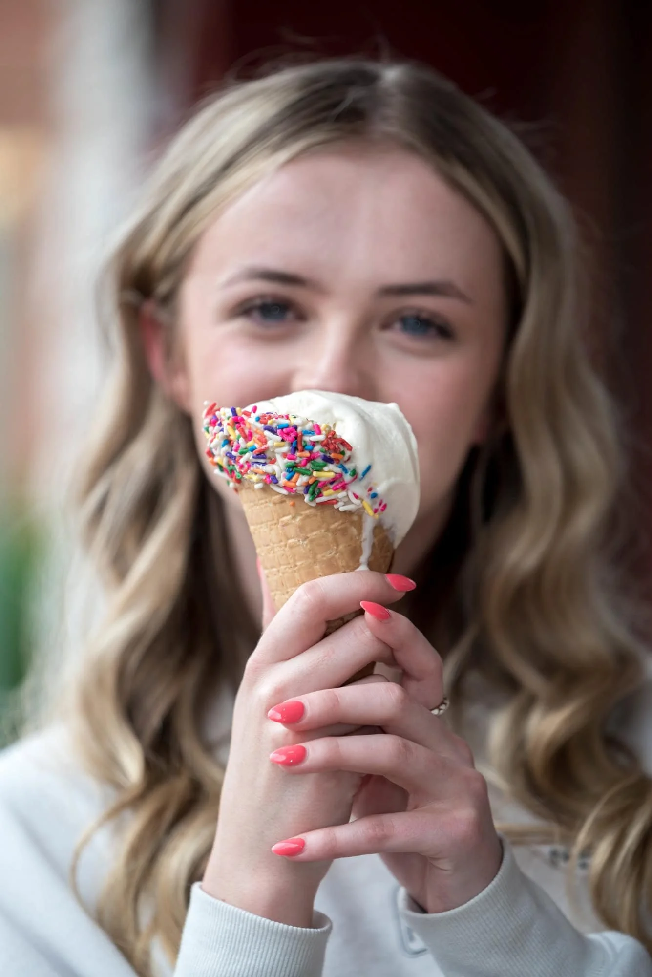 A picture captures a high school senior girl holding up a melting ice cream cone in front of her face while wearing a white sweatshirt outside an ice cream shop in St. Charles, MO.