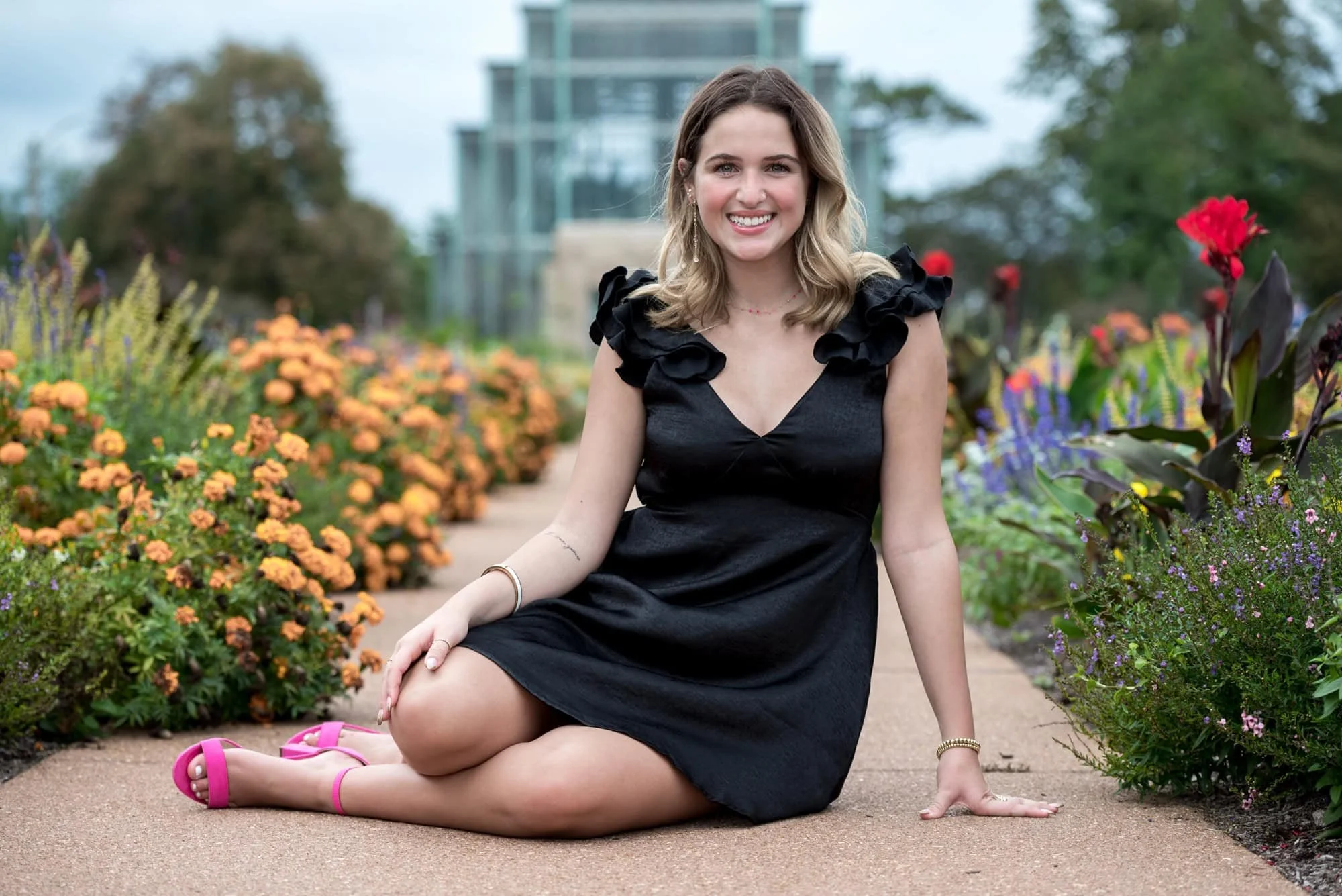 High school senior in a black dress and pink heels sitting on a garden pathway leading to the Jewel Box in St. Louis.