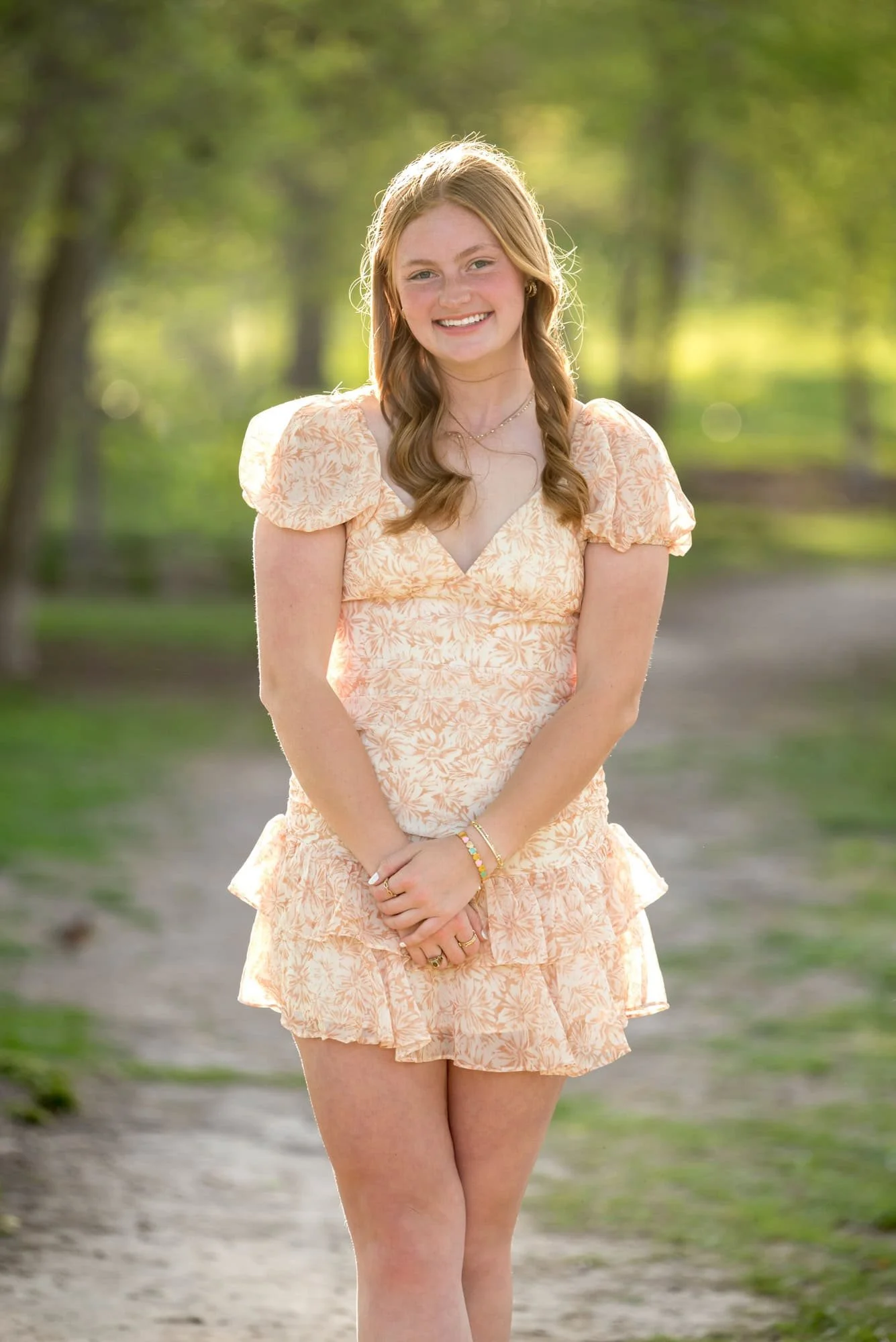 A picture captures a high school senior girl wearing an orange and white dress standing on the park grounds in St. Louis.