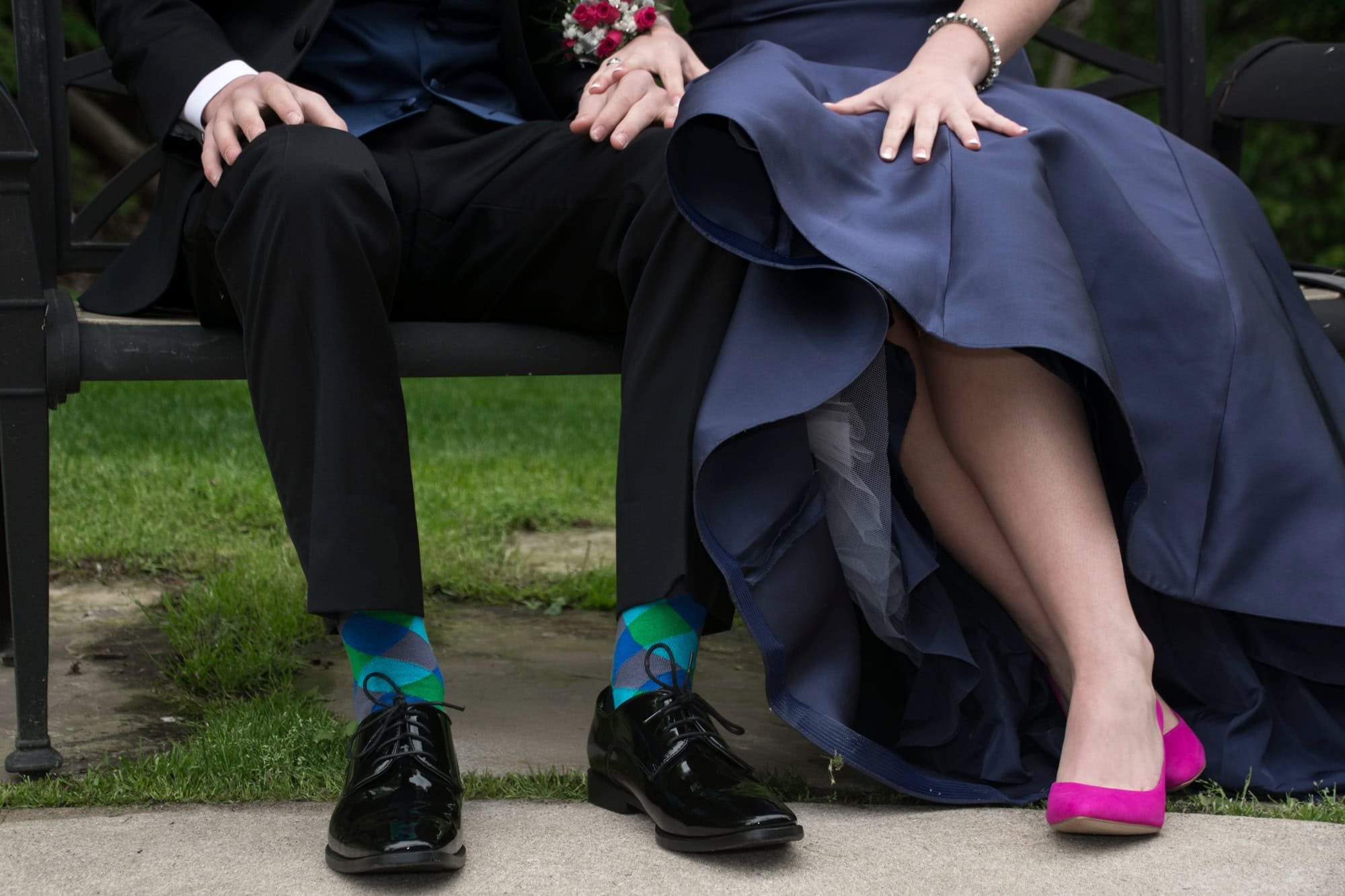 Close-up picture showing the fun details of a prom couple sitting on a bench, highlighting his blue and green argyle socks and her bright hot pink high heels taken by Monroe County senior photographer.