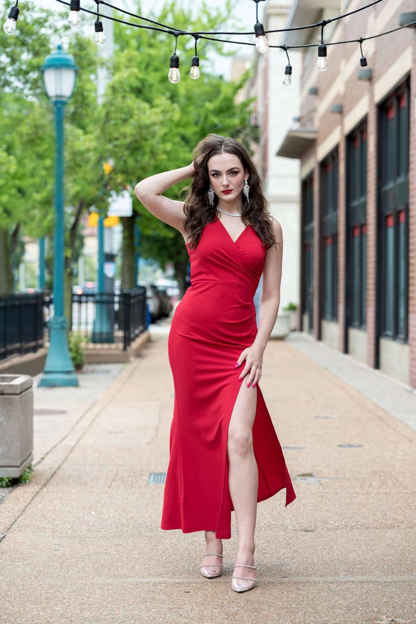 Standing on a local sidewalk in University City, a senior girl in a red long dress poses for a picture.