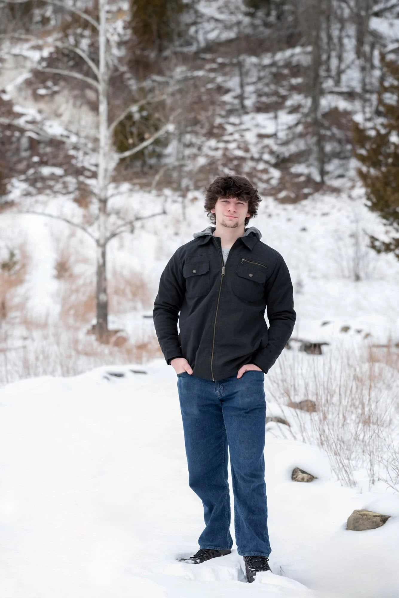 Winter senior photo of a high school boy on a snow-covered trail with a bare birch tree in the background taken by St. Charles County senior photographer.