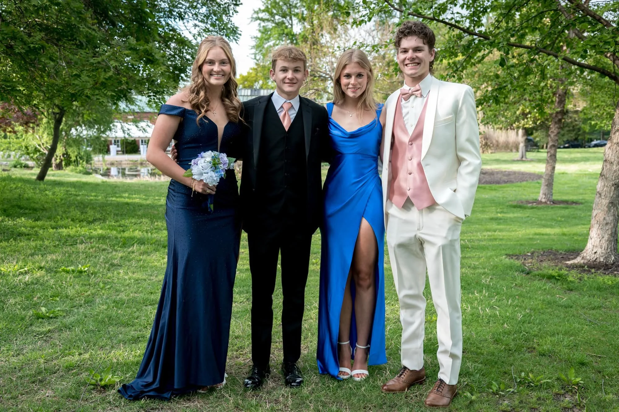 Standing in an open grassy park area in St. Louis, a senior girl poses with two guys and another girl for a group prom photo taken by a St. Louis senior photographer.