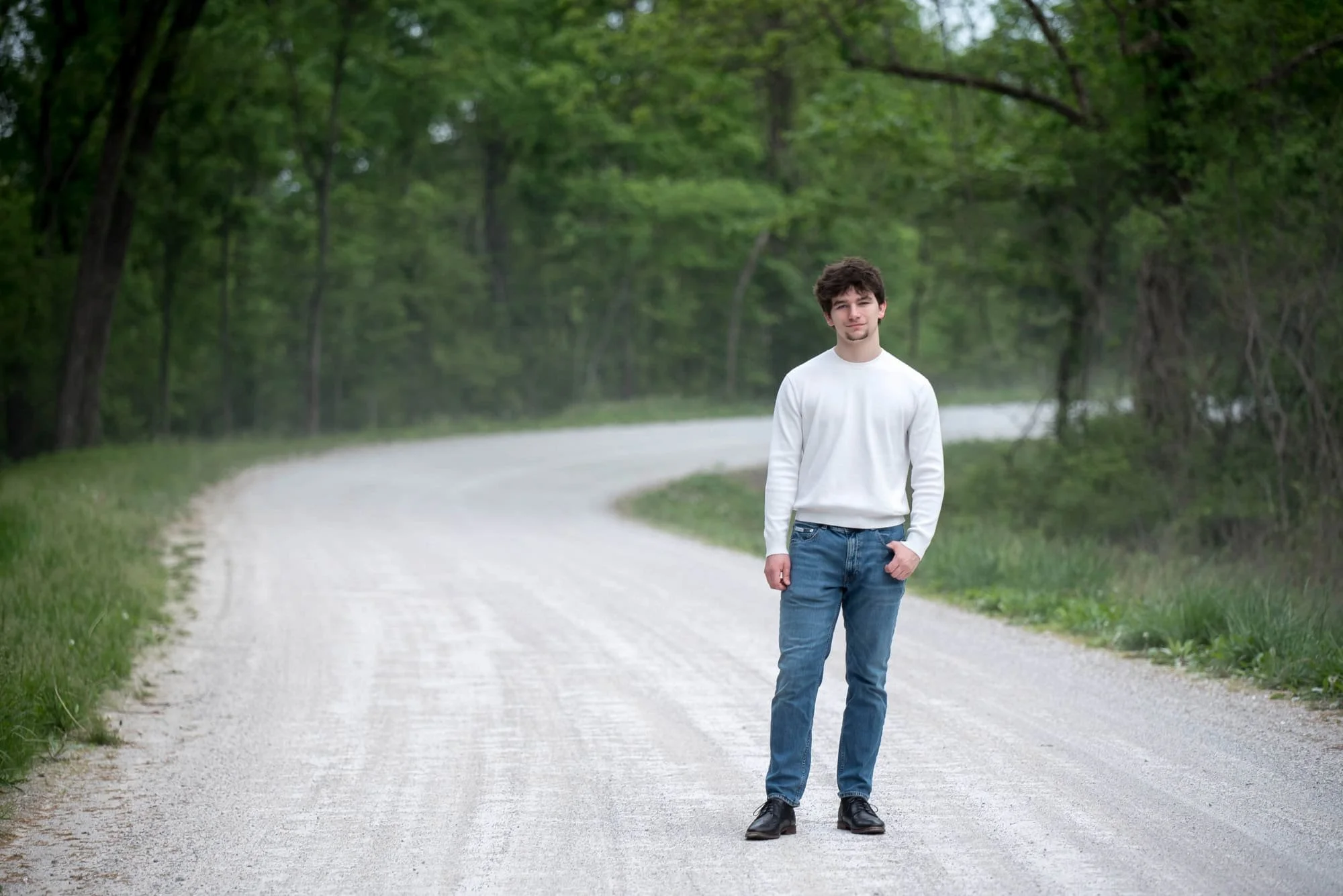 Senior guy standing on a gravel road in St. Charles County winding through a wooded conservation area during a senior photo session.
