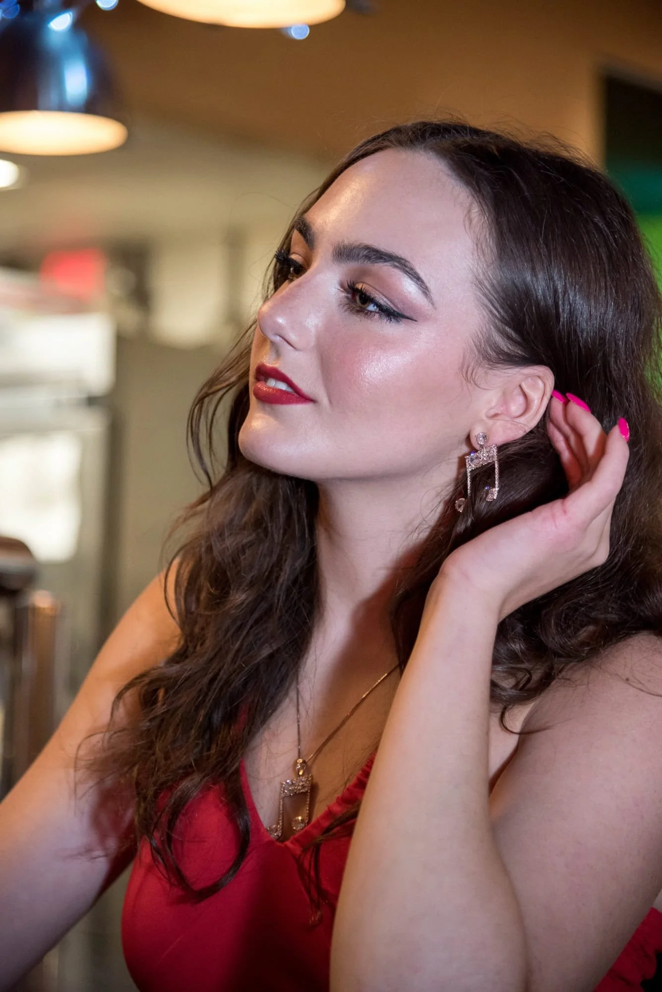 Showing her music note earring inside Fitz's in the Delmar Loop, a high school senior girl in a red tank top poses for a picture.