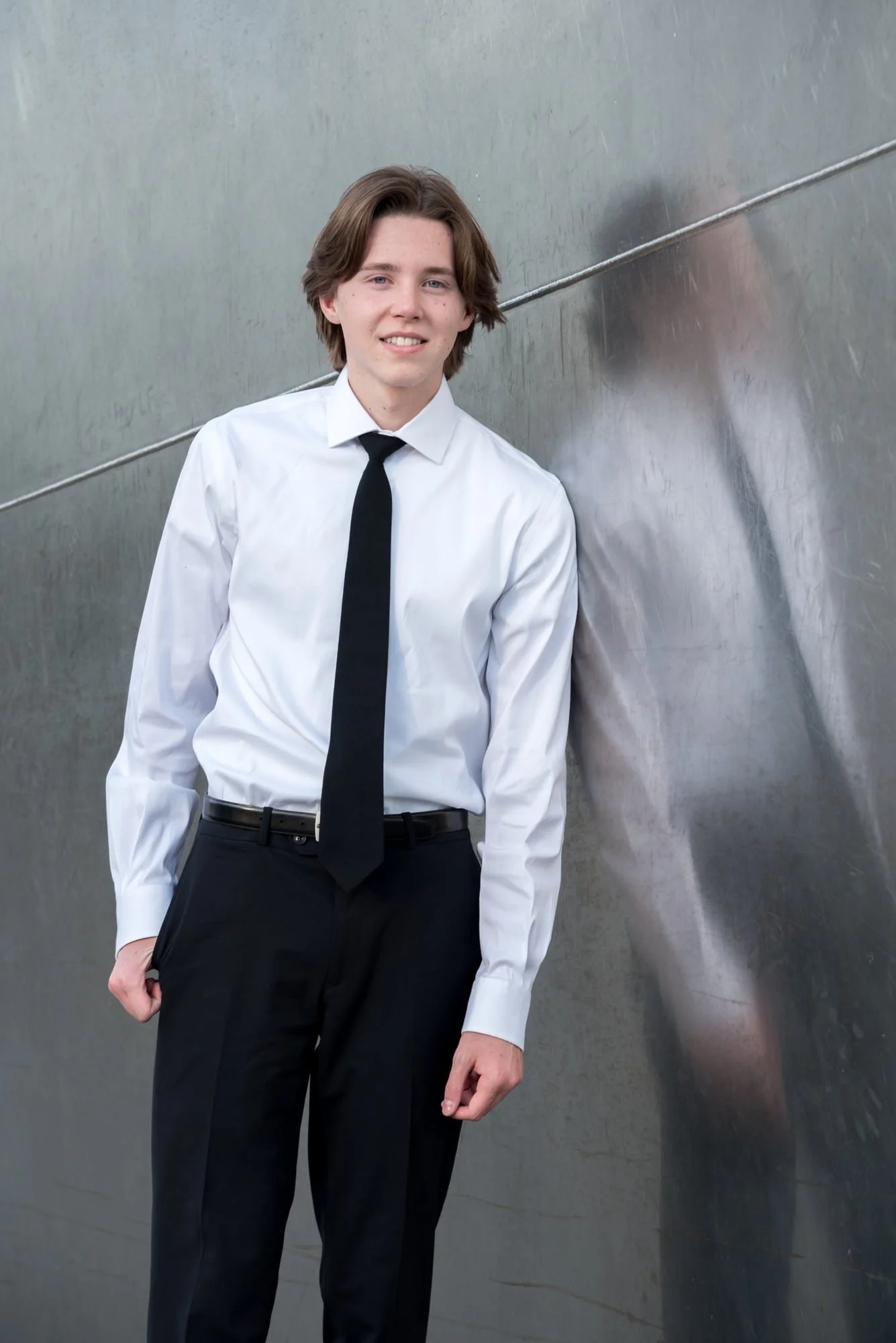 Creative architectural senior portrait featuring a graduate leaning against the stainless steel base of the Gateway Arch, showcasing a crisp reflection in the metal structure.