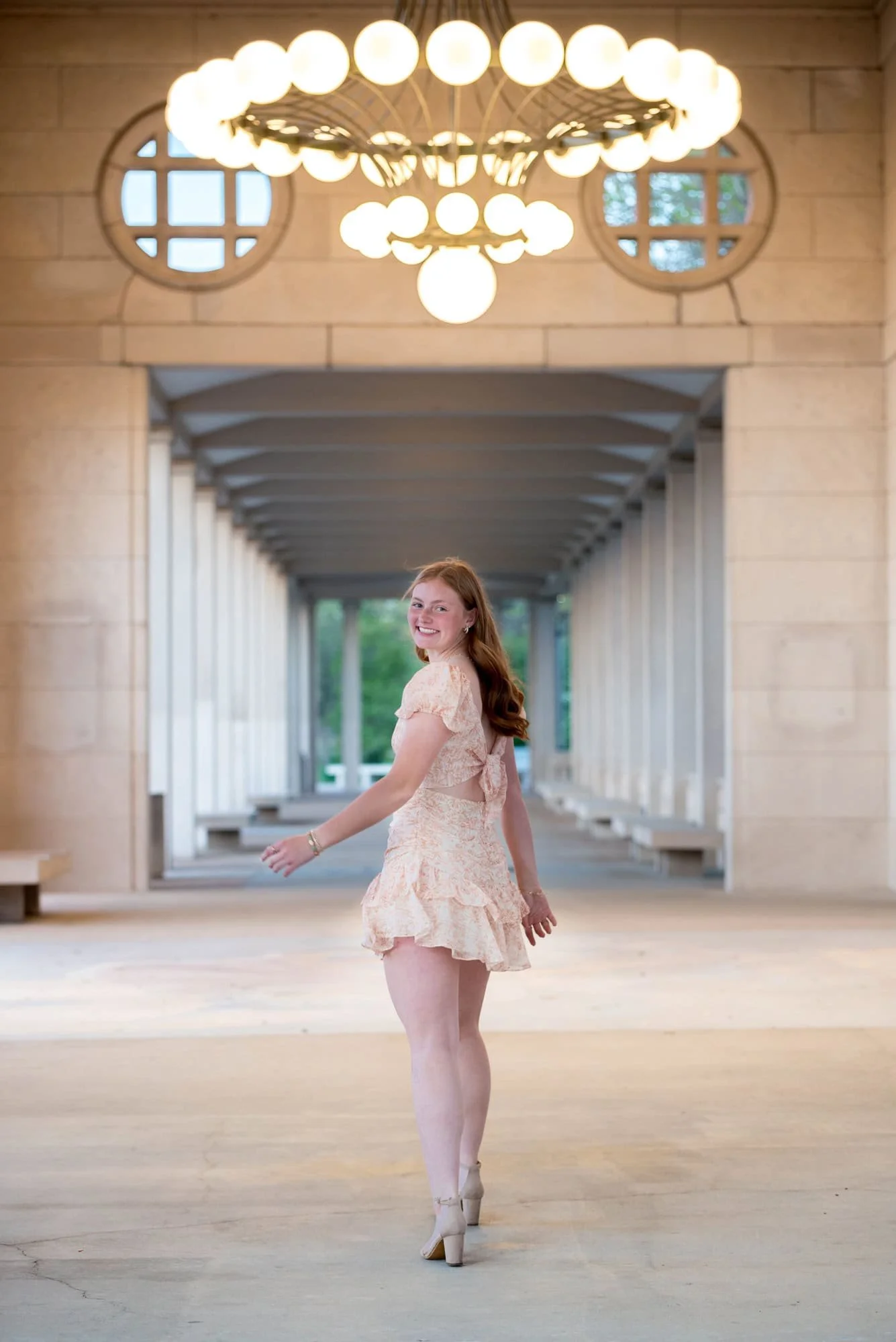 Twirling her orange and white dress to show movement, a senior girl poses for a photo outside at The Muny.