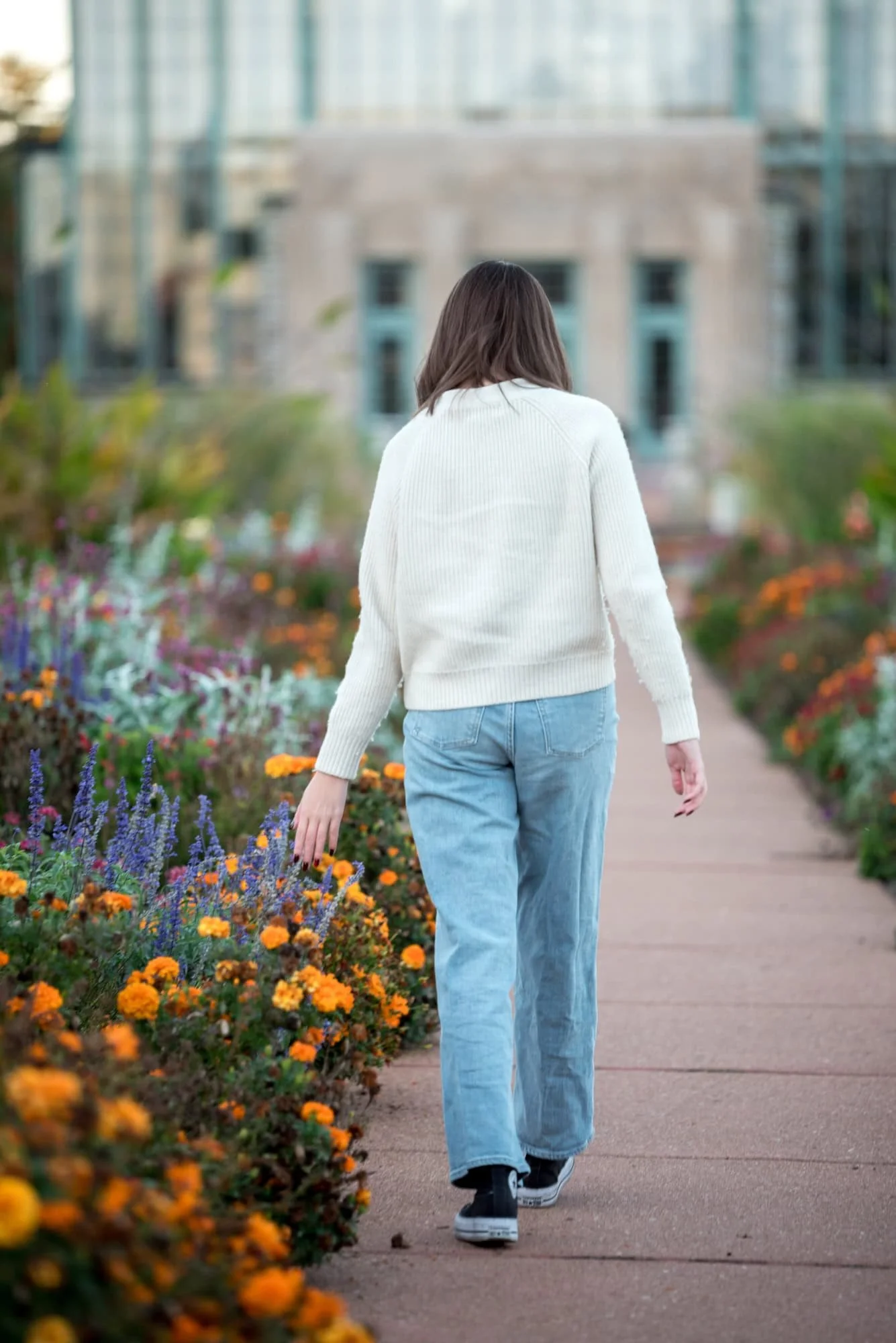 A senior girl walks along a scenic park path bordered by lush garden flowers during a whimsical St. Louis senior session.