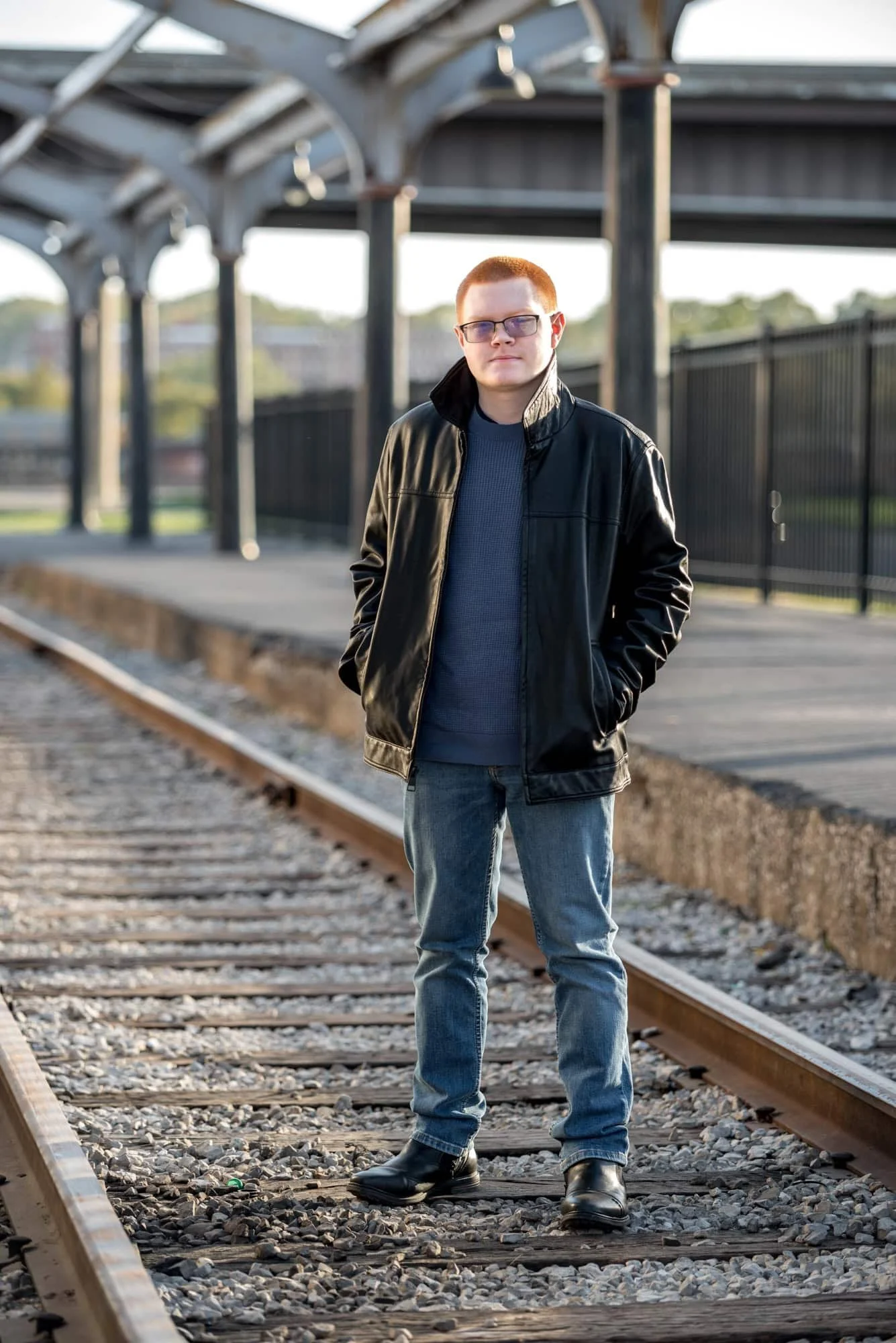 Moody urban style photo showing a boy with a serious look standing on the train tracks with his hands in his pockets taken by St. Louis County senior photographer.