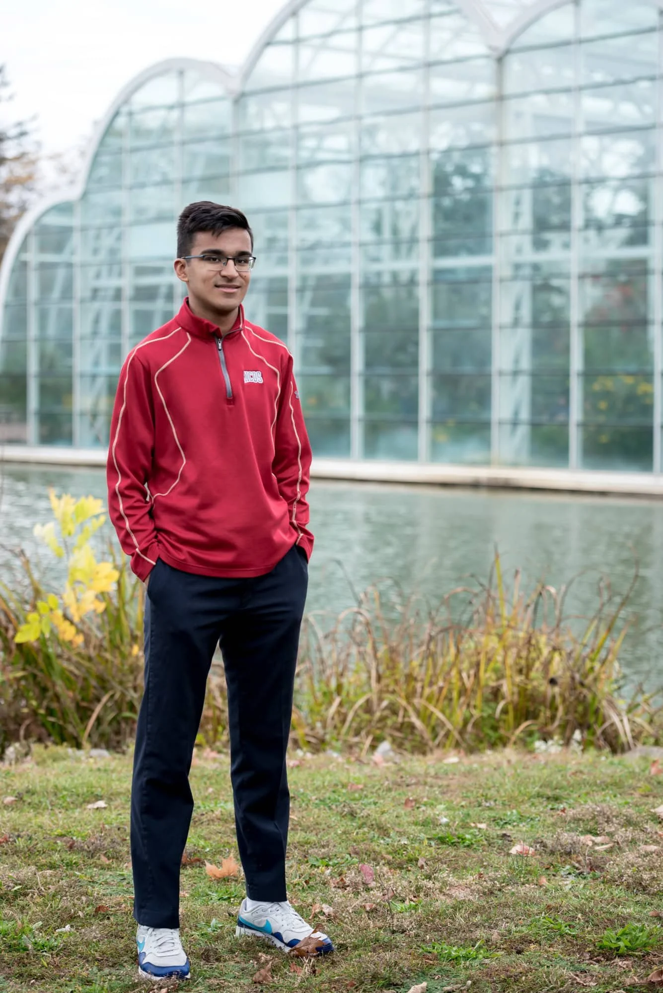 Casual senior portrait of a guy standing in the grass with his hands in his pockets in front of the Butterfly House pond in Chesterfield.