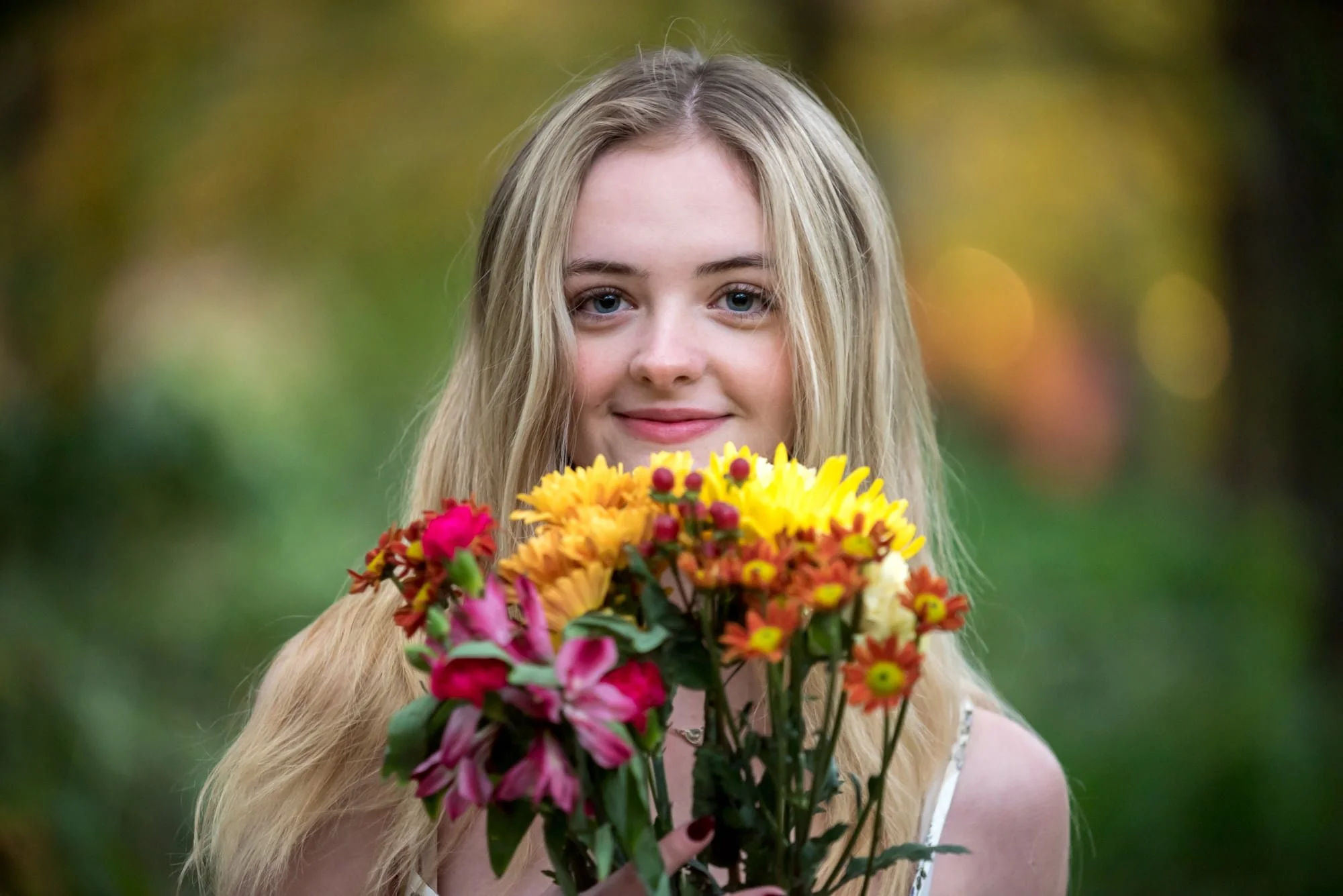 A senior girl in St. Louis, MO stands in front of blurred out fall colors holding up a bouquet of flowers in front of her face for a picture.