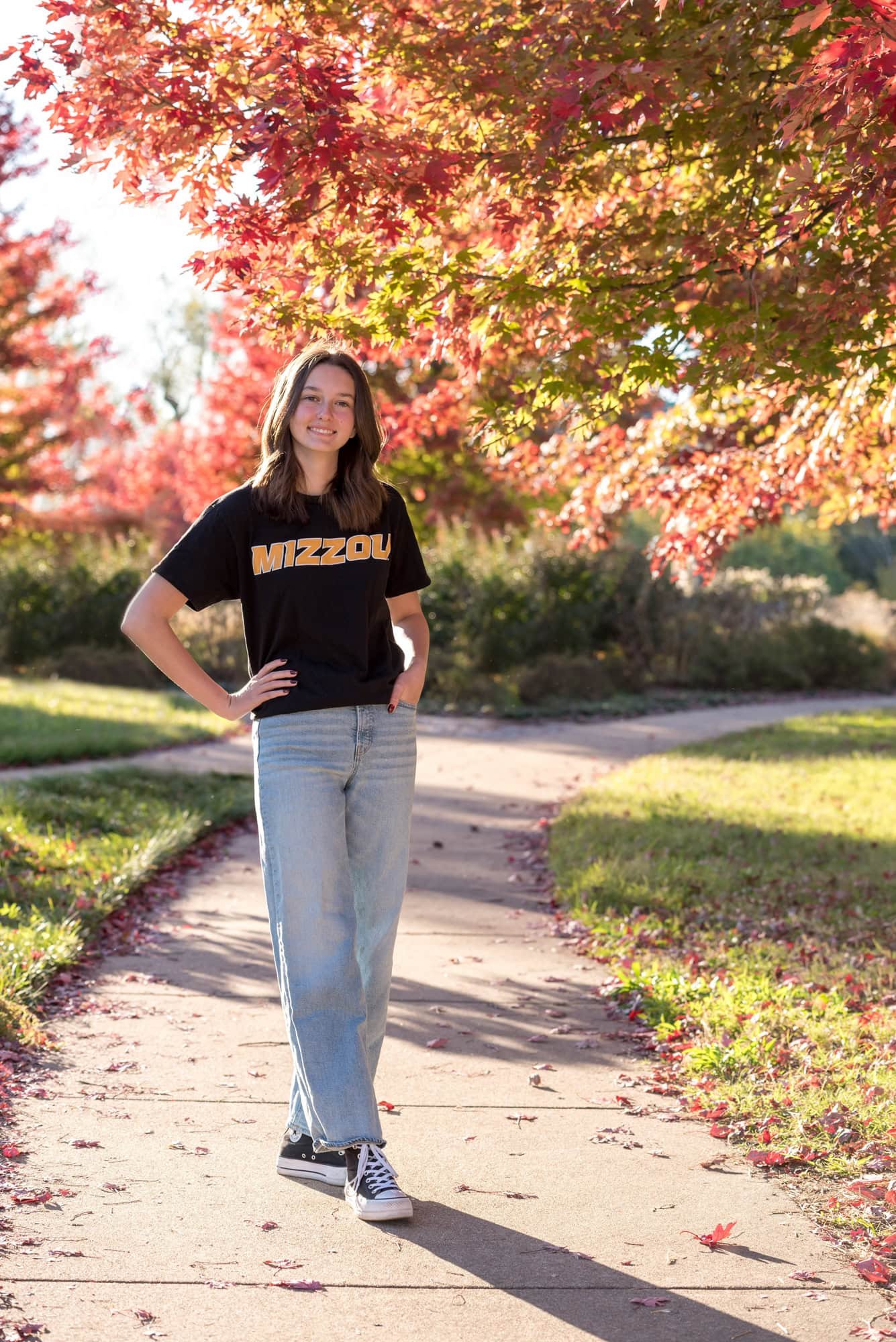A senior girl smiles on a paved park path during the fall across from The Muny for a Mizzou College picture.