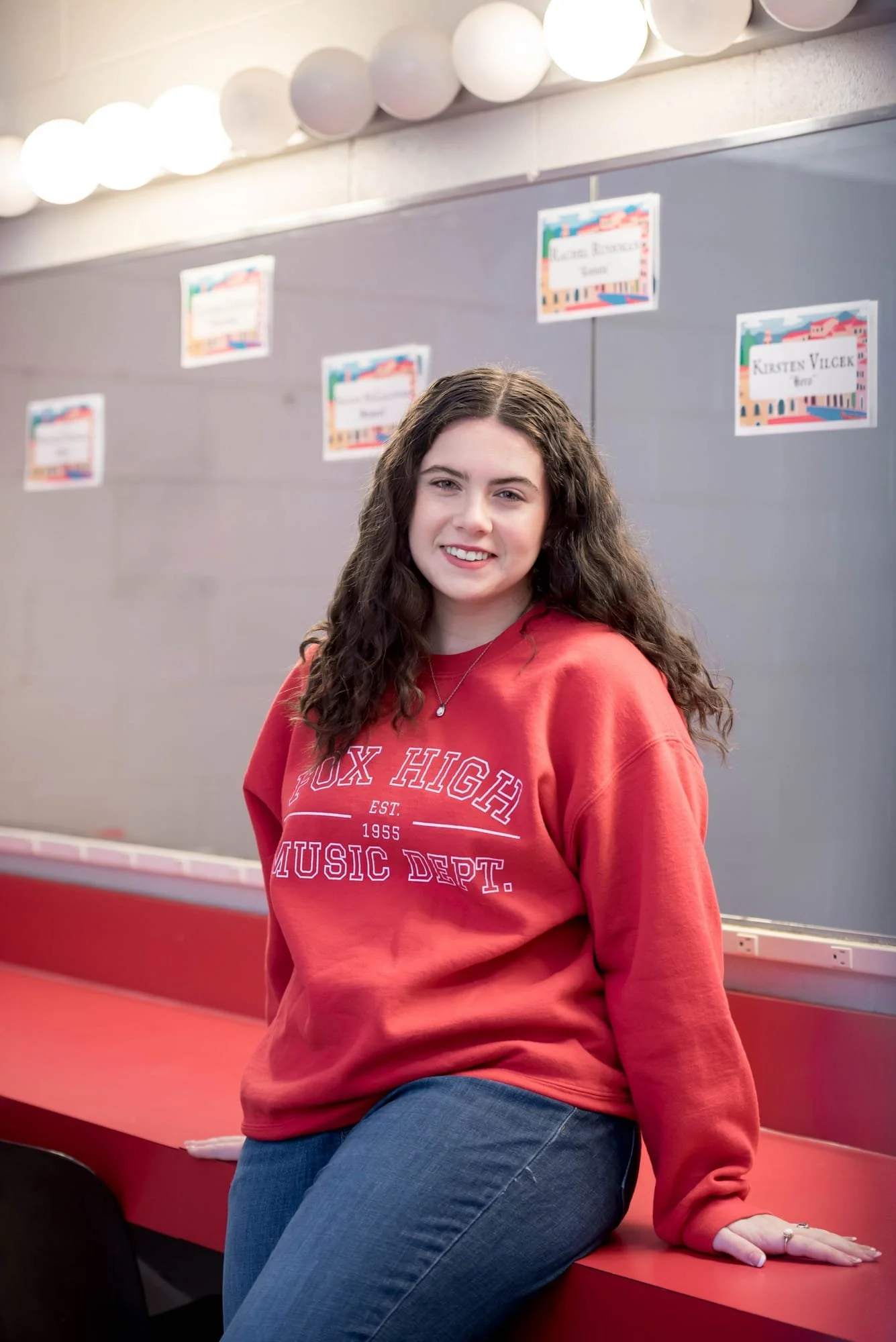 A photo inside the Rickman Auditorium dressing room shows a high school senior girl wearing a red Fox High School music department sweatshirt and blue jeans.