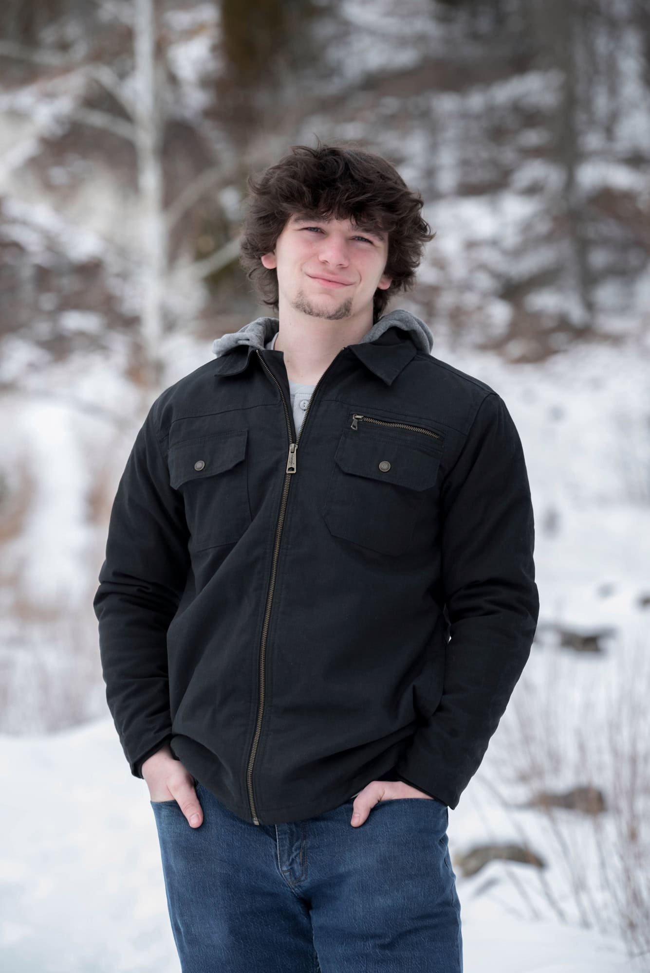 High school boy in blue jeans and a heavy black jacket on a snowy path at Klondike Park.
