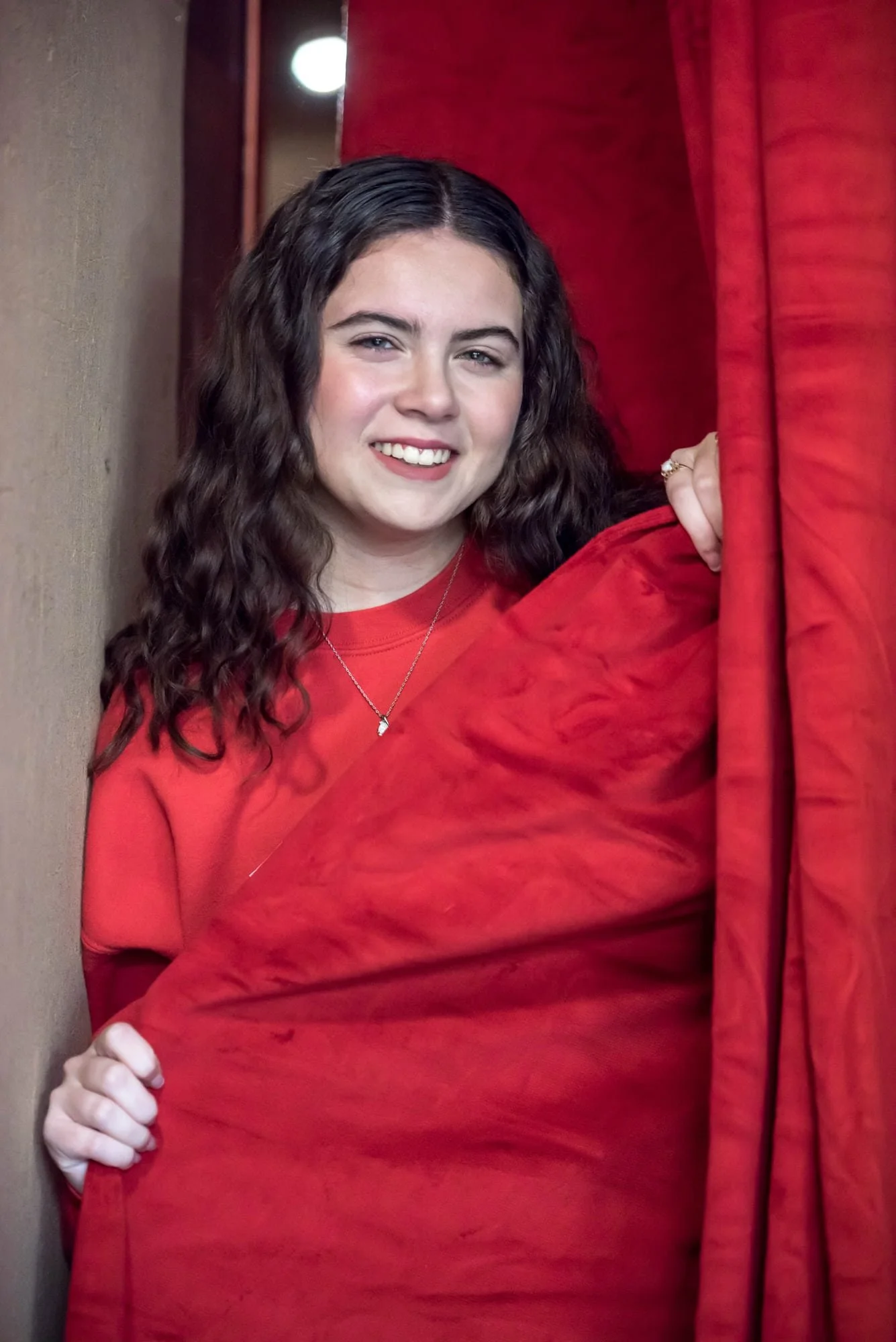 A picture captures a high school senior girl wearing a red Fox High School sweatshirt next to the theater curtains in Jefferson County.