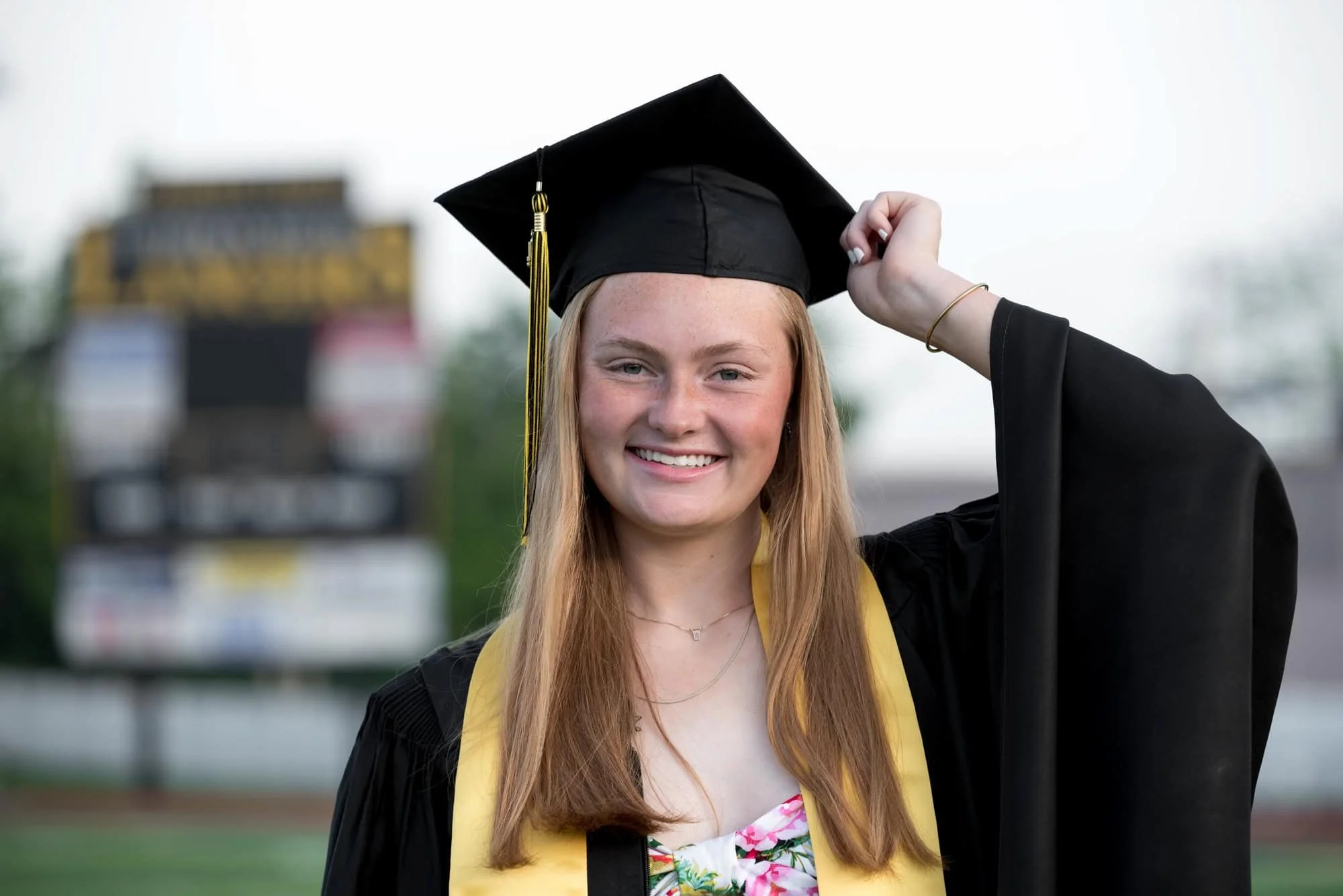 A picture captures a senior girl wearing a black graduation gown and gold stole on the school football field in St. Louis County.