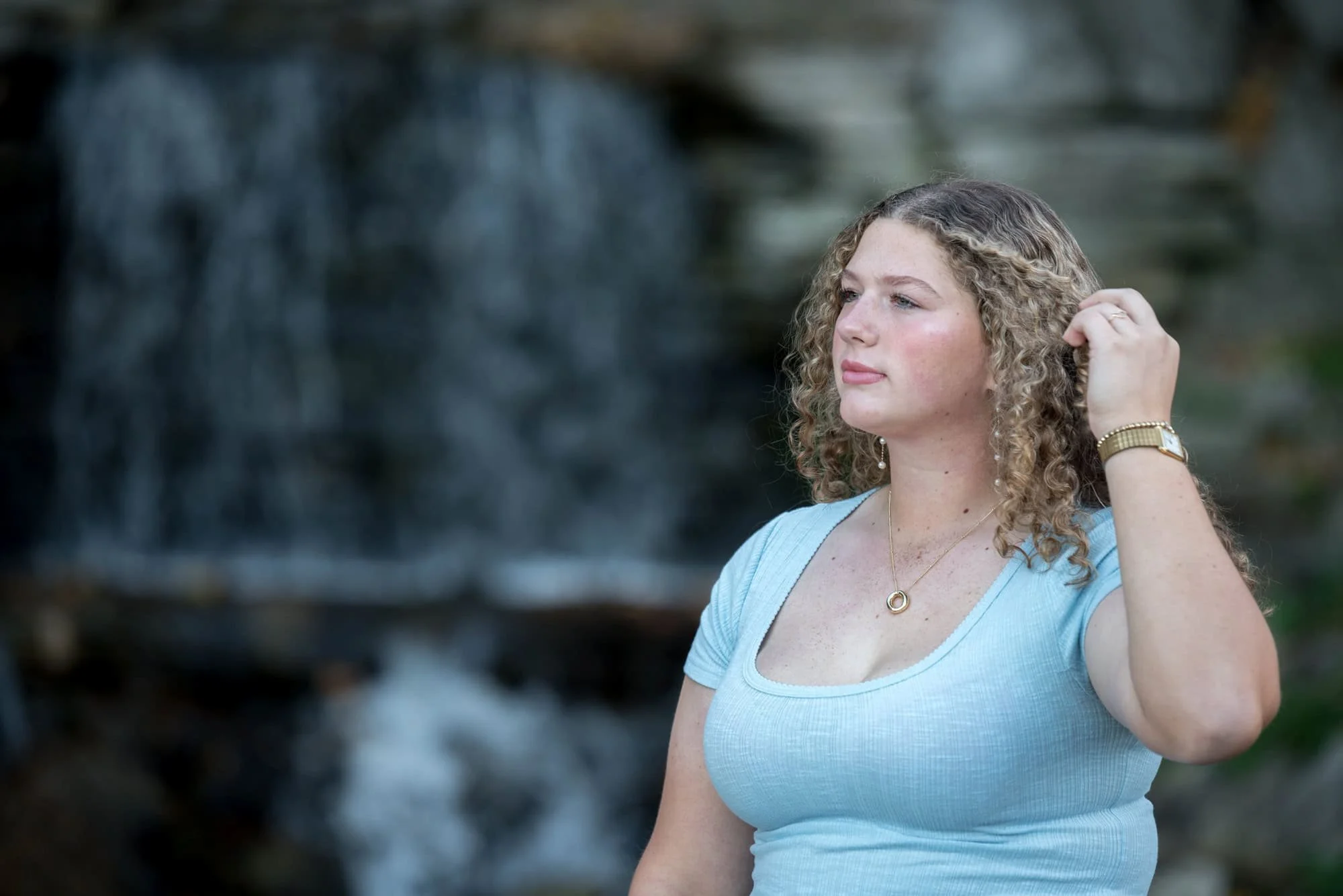 Senior photo located at the rocky Forest Park waterfall showing a girl playfully running her fingers through her hair.