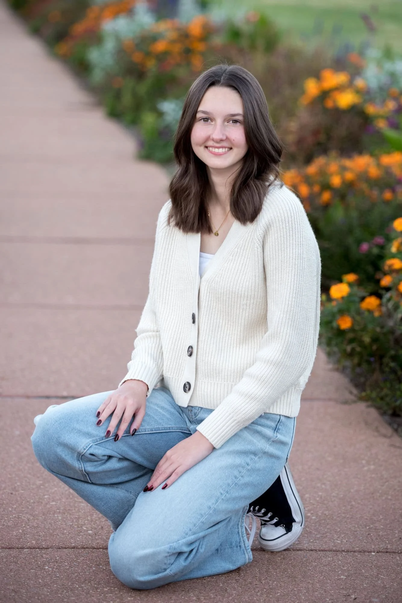 A high school senior girl sits on a stone pathway surrounded by blooming orange flowers for a Jewel Box picture.