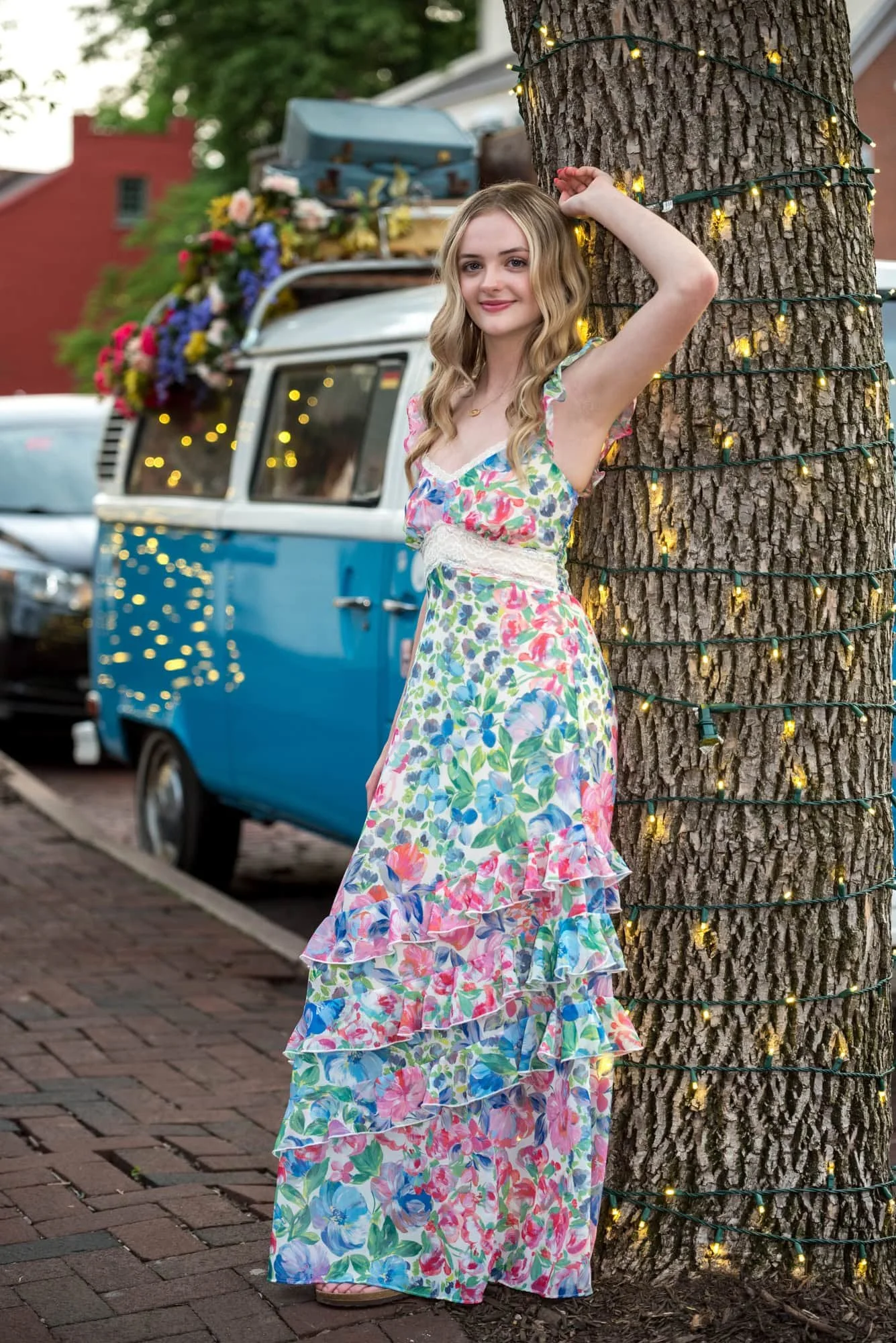 Posing next to a vintage VW bus in old town St. Charles, a senior girl in a floral long dress smiles for a photo.