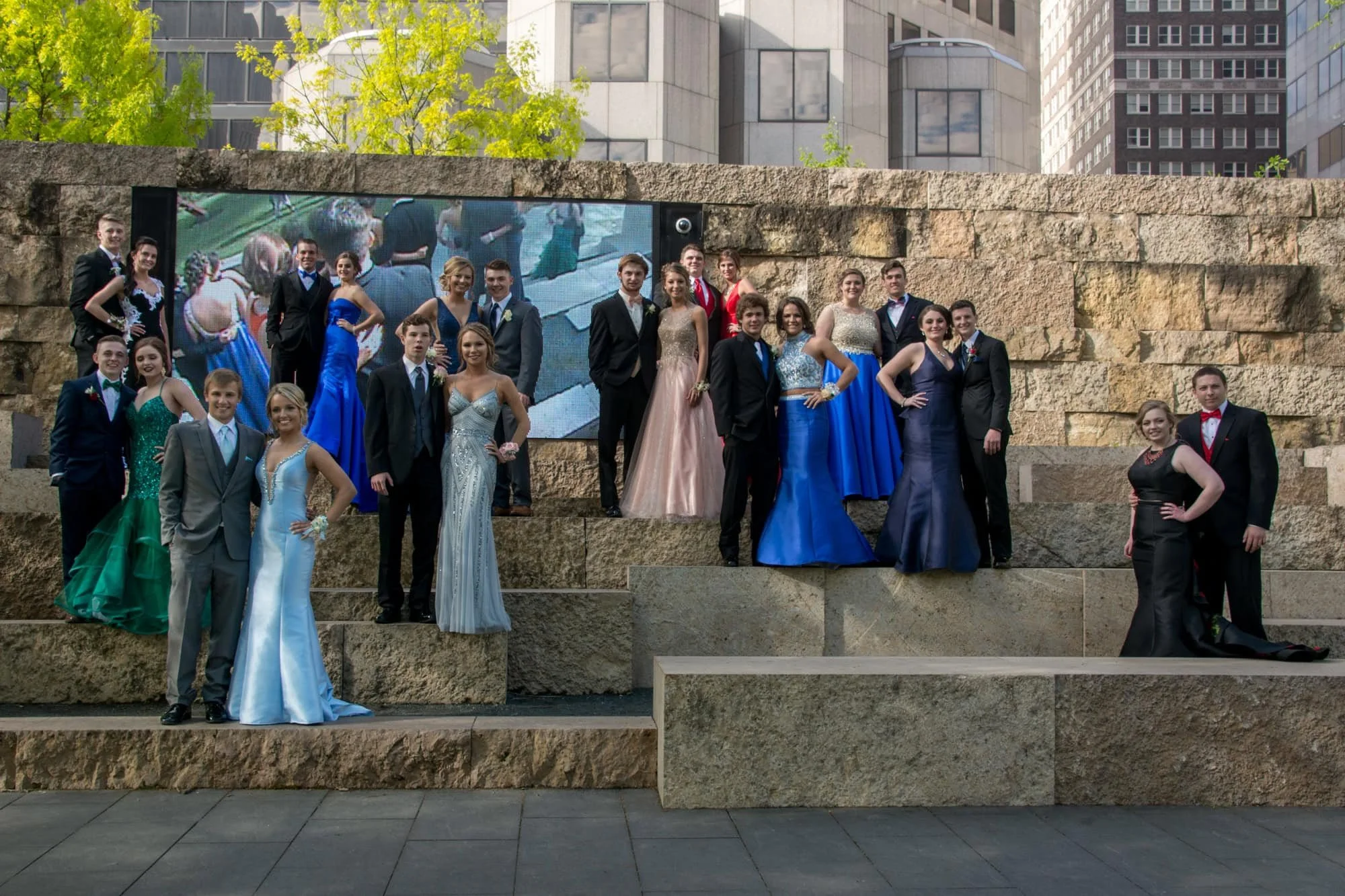 A large group of high school students in prom attire posing together on stone steps at Citygarden in St. Louis, Missouri.