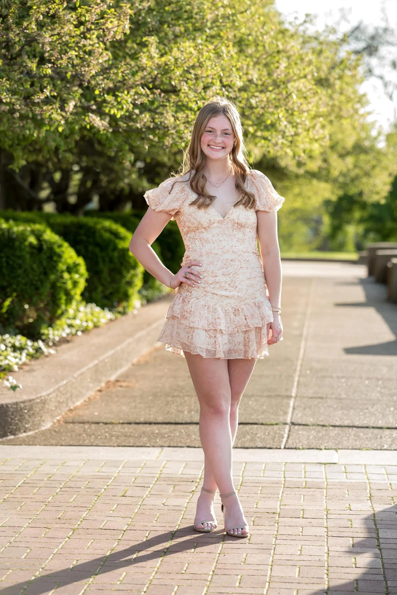 Standing on the garden pathway at the World's Fair Pavilion, a senior girl in an orange and white dress smiles for a photo.
