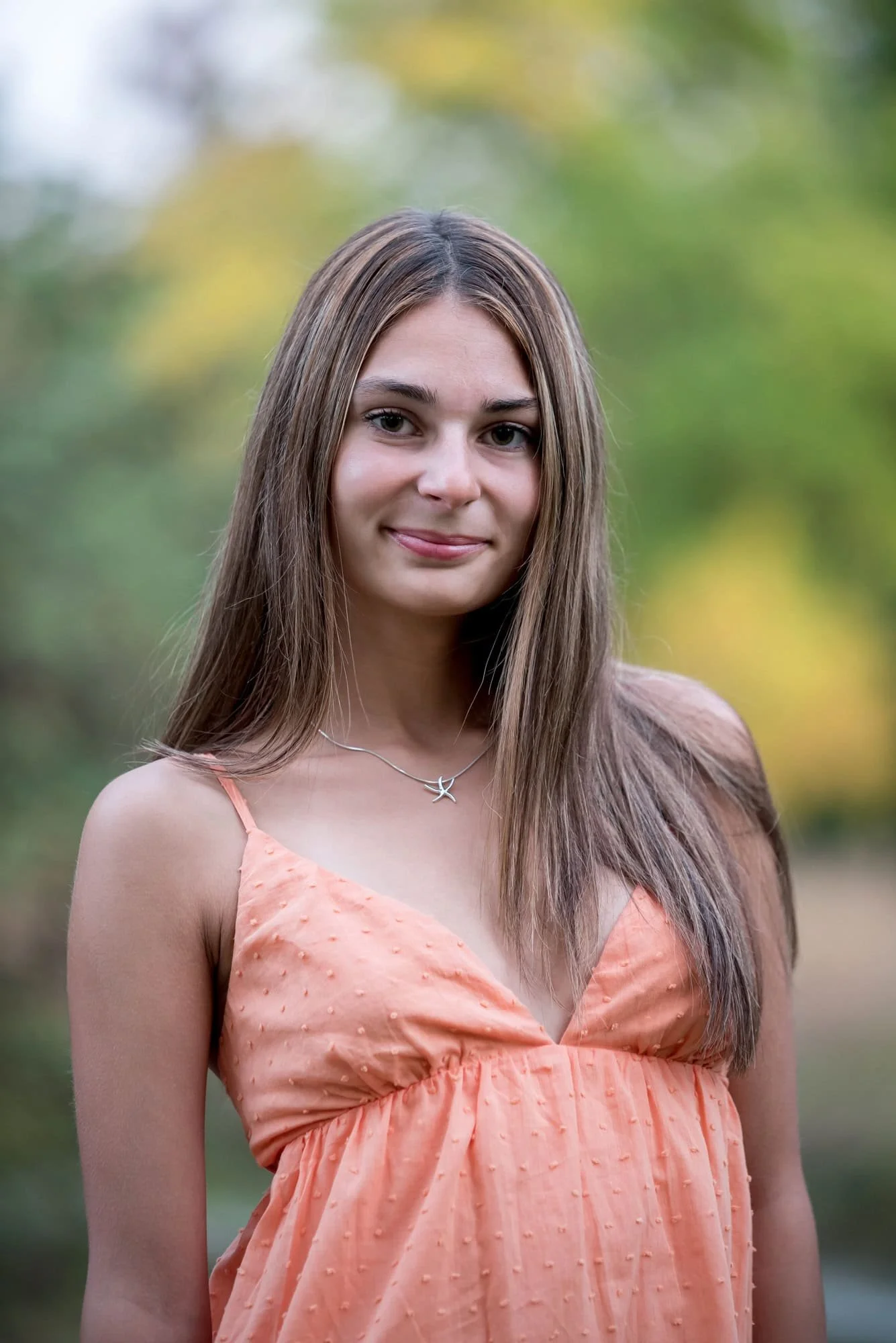 Bright and colorful close-up high school senior picture in Forest Park highlighting a smiling girl wearing a vibrant short orange dress.