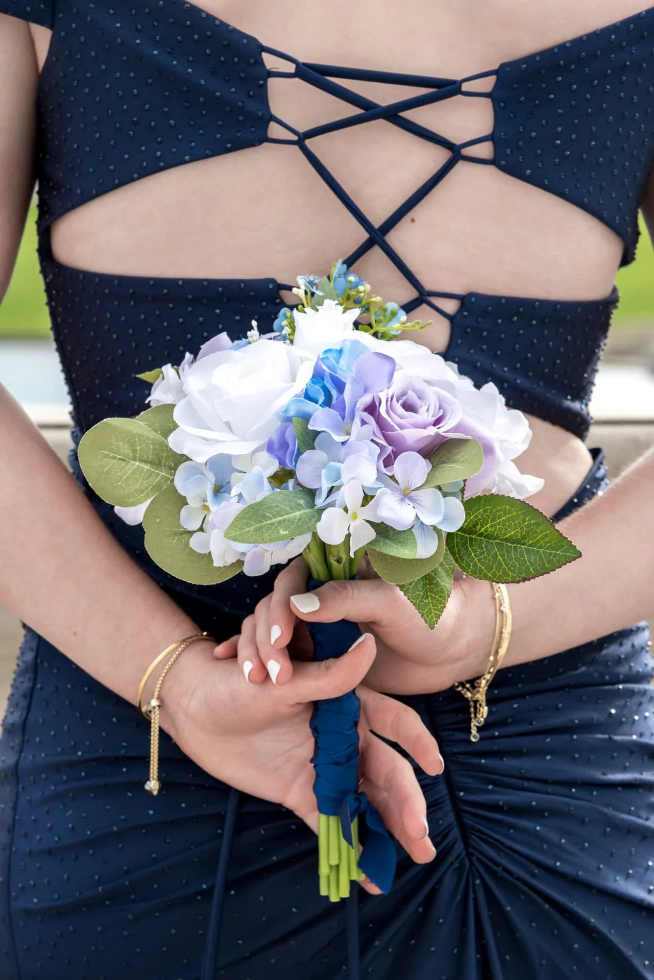 Holding her flower bouquet behind her back, a senior girl in a navy blue prom dress poses for a picture taken by a St. Louis senior photographer.