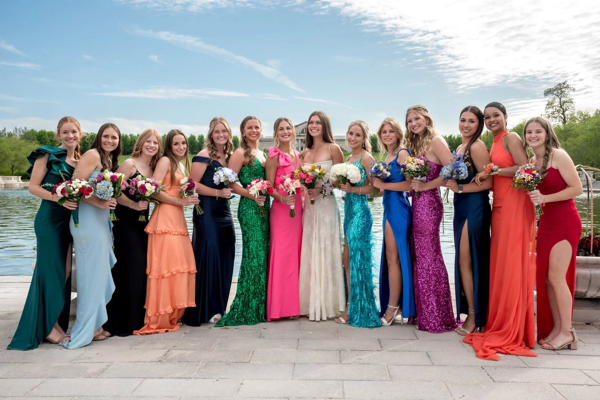 A photo captures a group of high school senior girls in colorful dresses holding their flower bouquets outside on Art Hill.