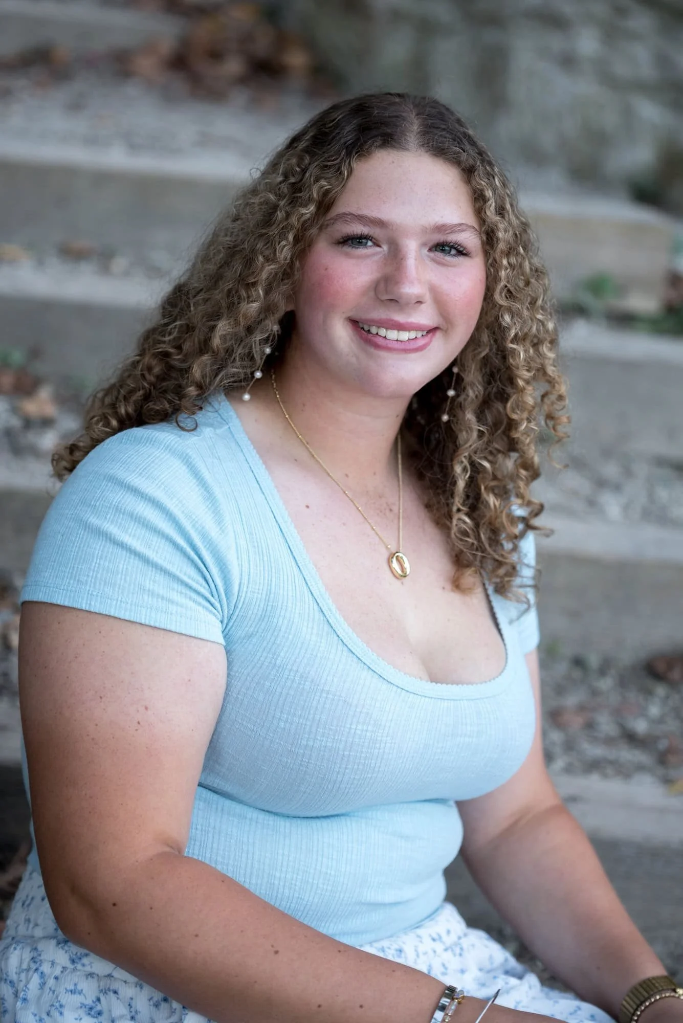 Close-up photo located on the steps of the Forest Park waterfall featuring a senior sitting relaxed in a short-sleeve blue shirt.