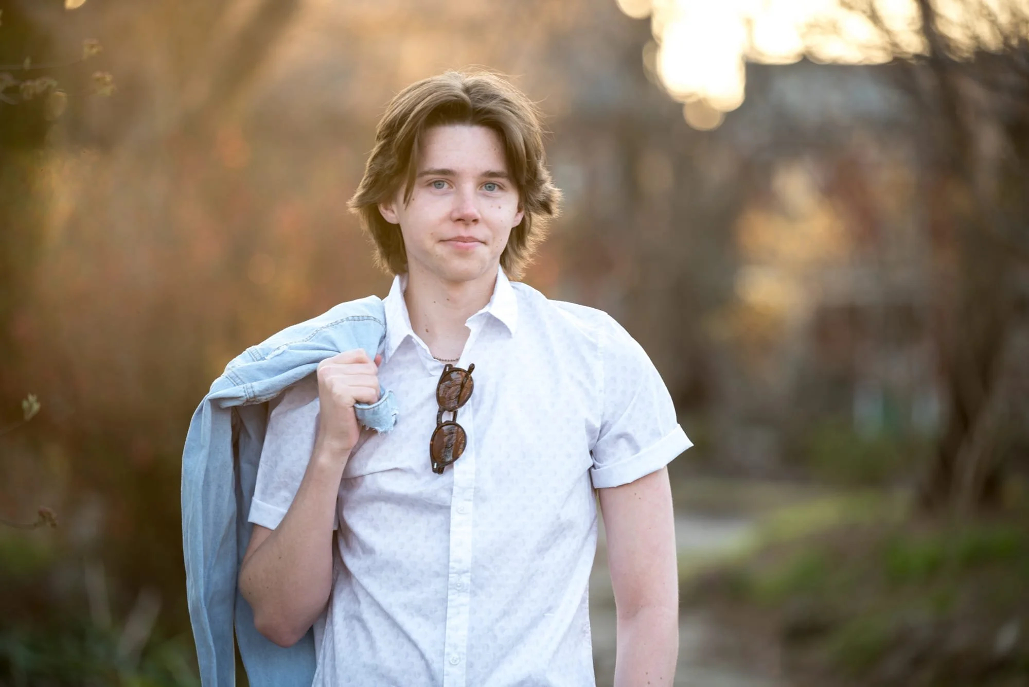 Senior photo located at Lafayette Square capturing a boy walking along a pathway with sunglasses hanging on his white t-shirt and his plaid shirt slung over his shoulder.
