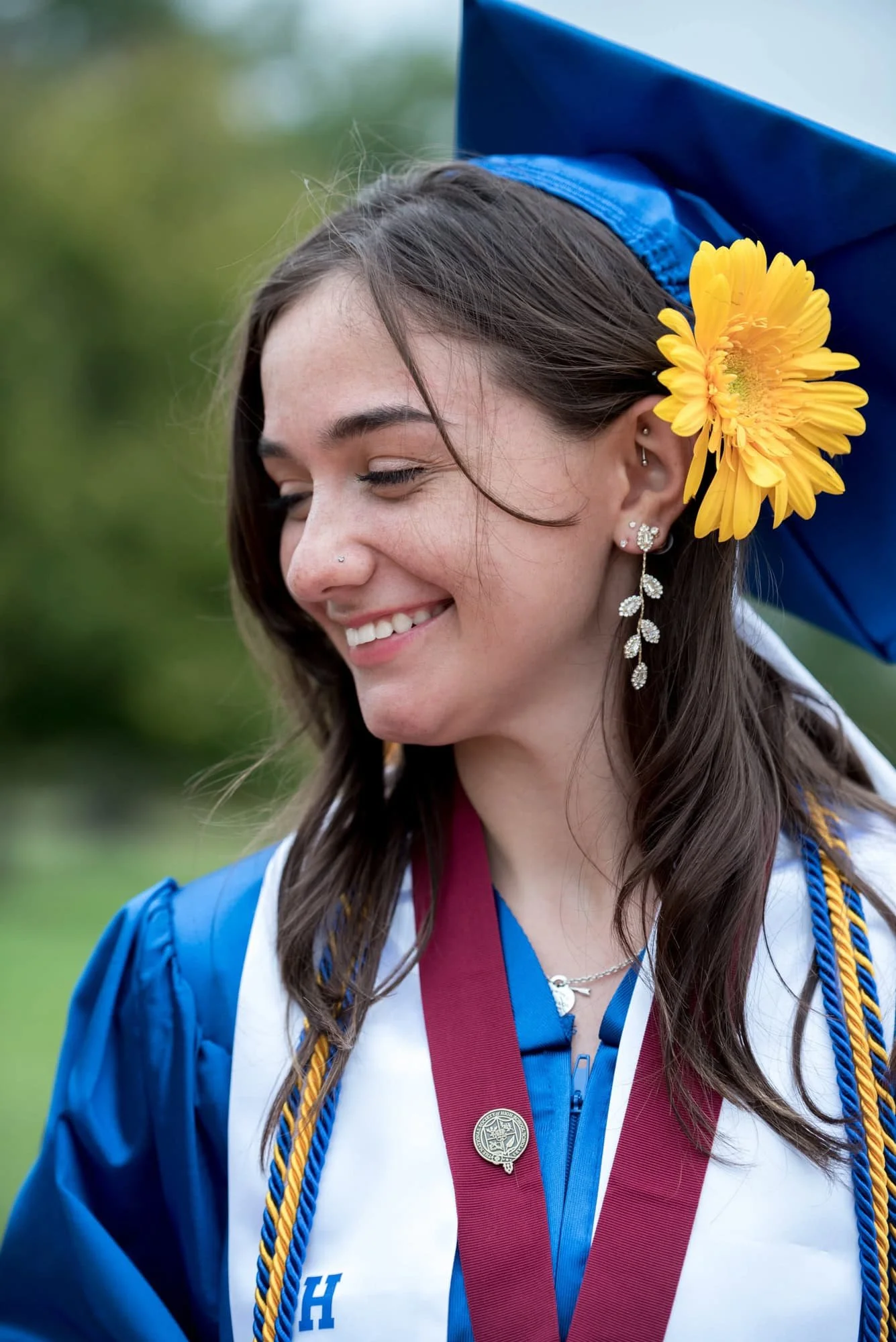 A picture captures a senior girl wearing a blue graduation cap with a yellow flower in her hair as she looks away from the camera, taken by a St. Louis photographer.