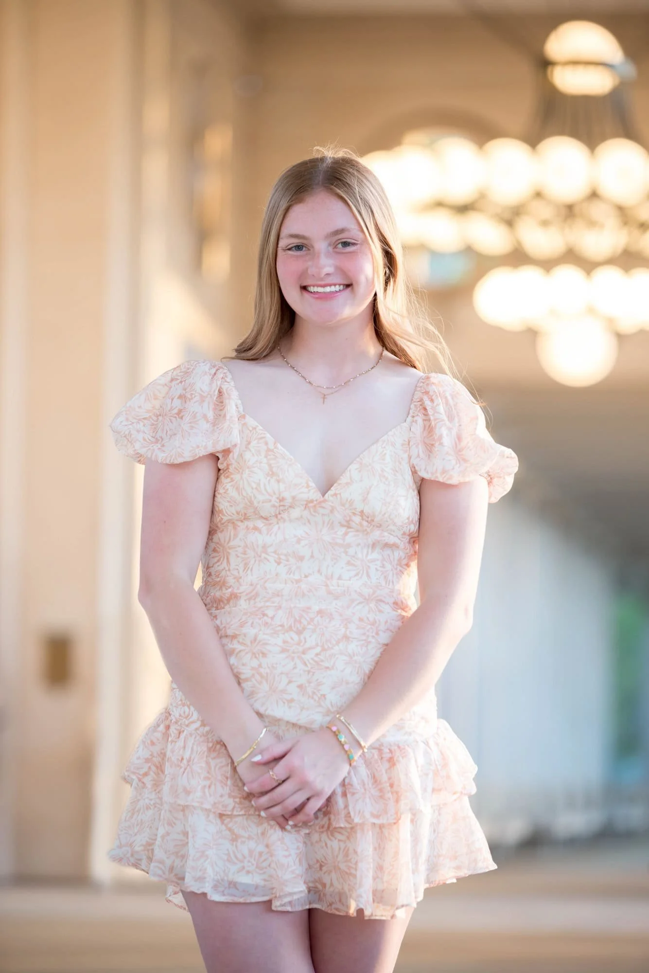 Wearing an orange and white dress, a senior girl stands under the covered walkways at The Muny for a picture.