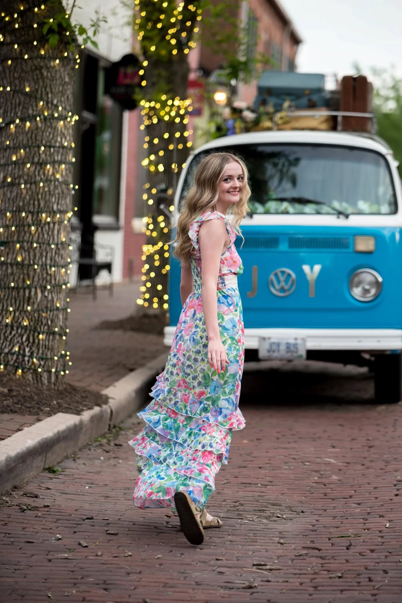 Running towards a vintage Volkswagen teal bus, a senior girl in a floral long dress smiles for a spring picture, taken by St. Charles County photographer.