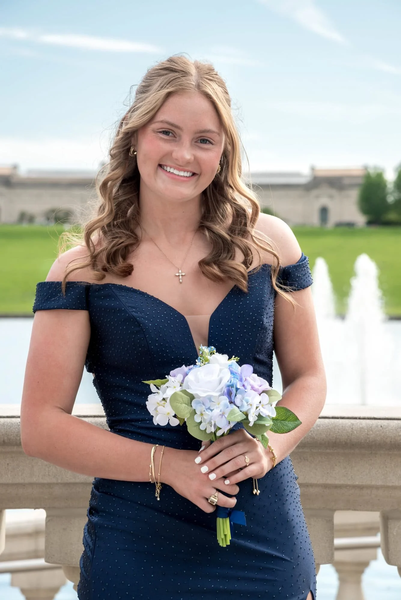Standing in front of the lake basin at Art Hill in Forest Park, a senior girl in a navy blue dress holds her bouquet for a prom picture.