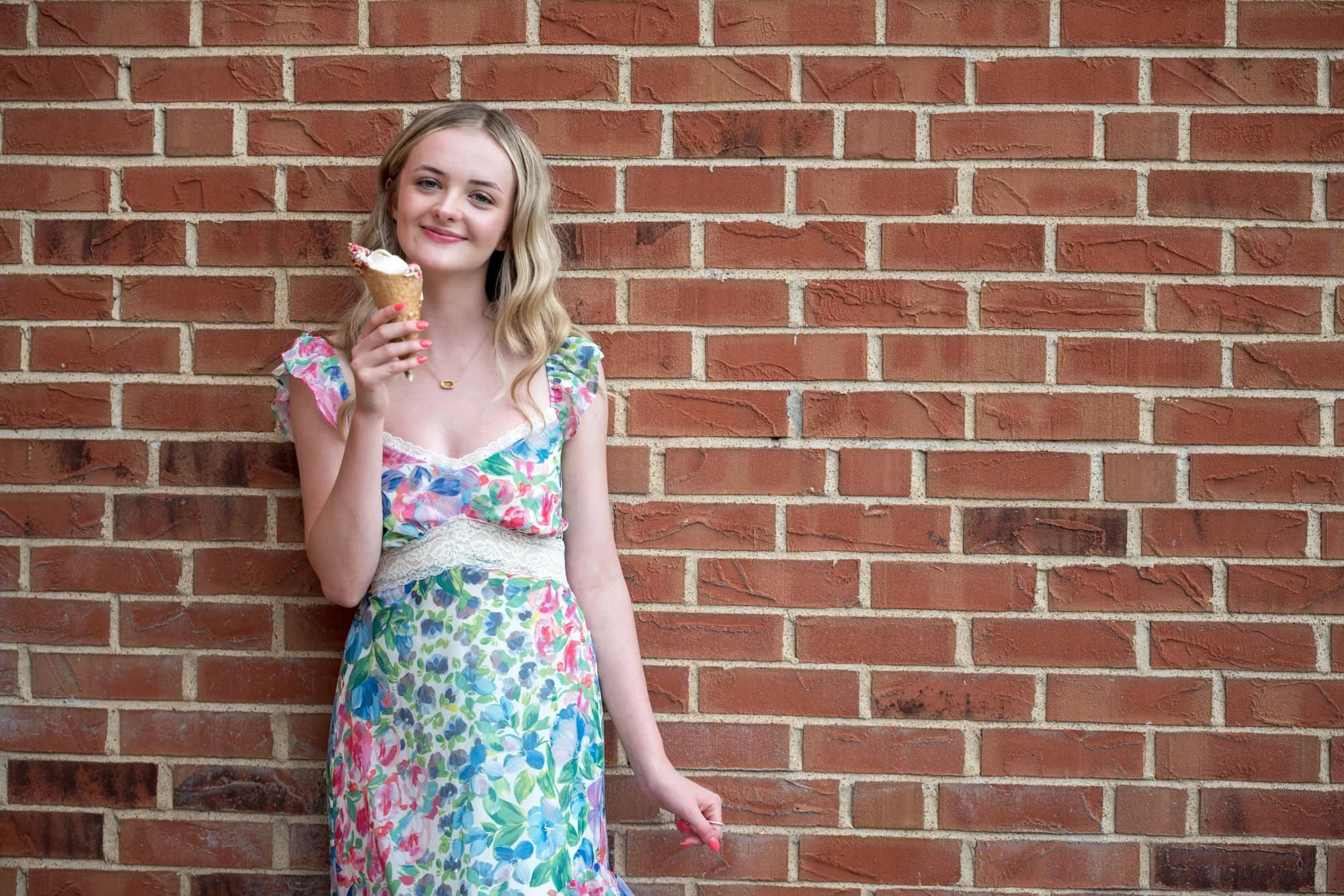 Holding an ice cream cone, a senior girl wearing a floral long dress poses for a spring picture taken by a St. Charles senior photographer.