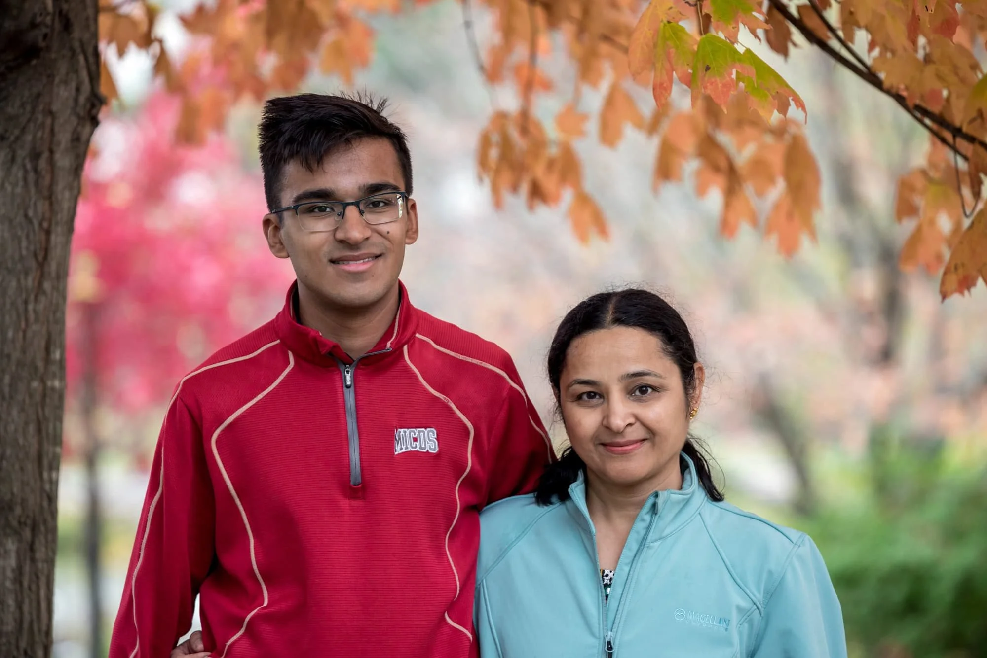 Heartwarming close-up portrait of a senior guy and his mom smiling together under a vibrant orange autumn tree during a fall portrait session in Chesterfield MO.