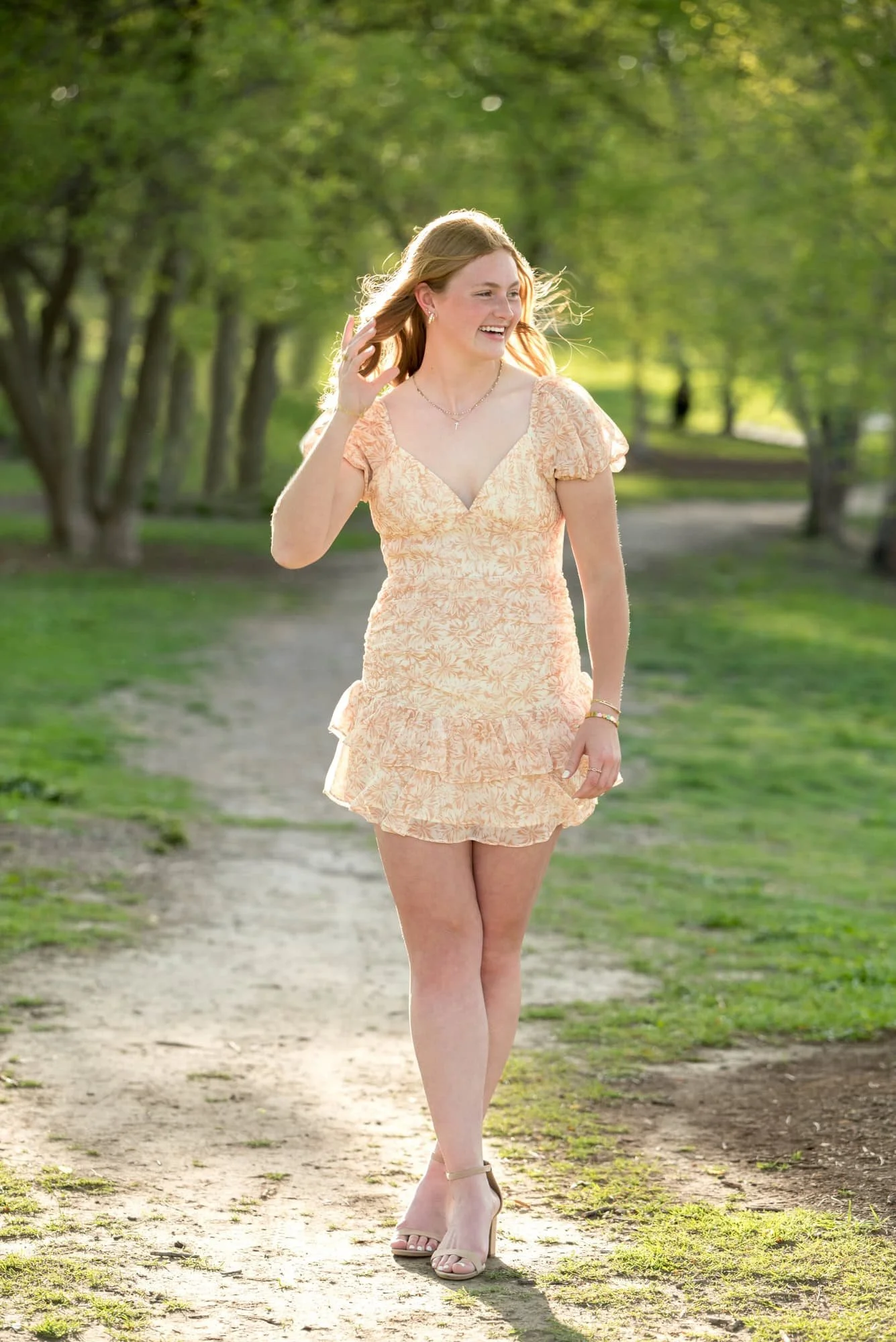 Grinning during a hair toss, a high school senior girl in an orange and white dress poses for an outdoor photo in St. Louis.