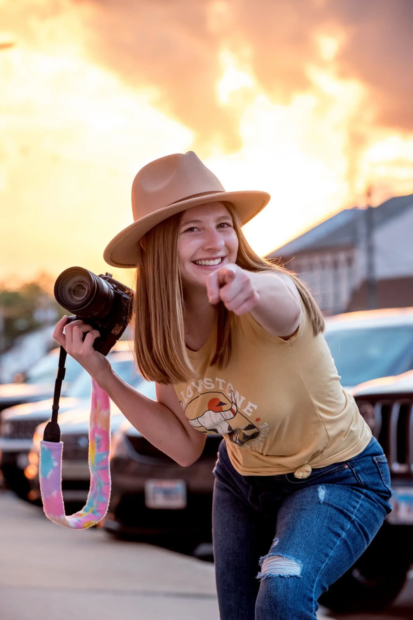 A picture of Amanda owner of Amanda Photography pointing excited at the camera while holding a camera during sunset in the city of Waterloo, IL.