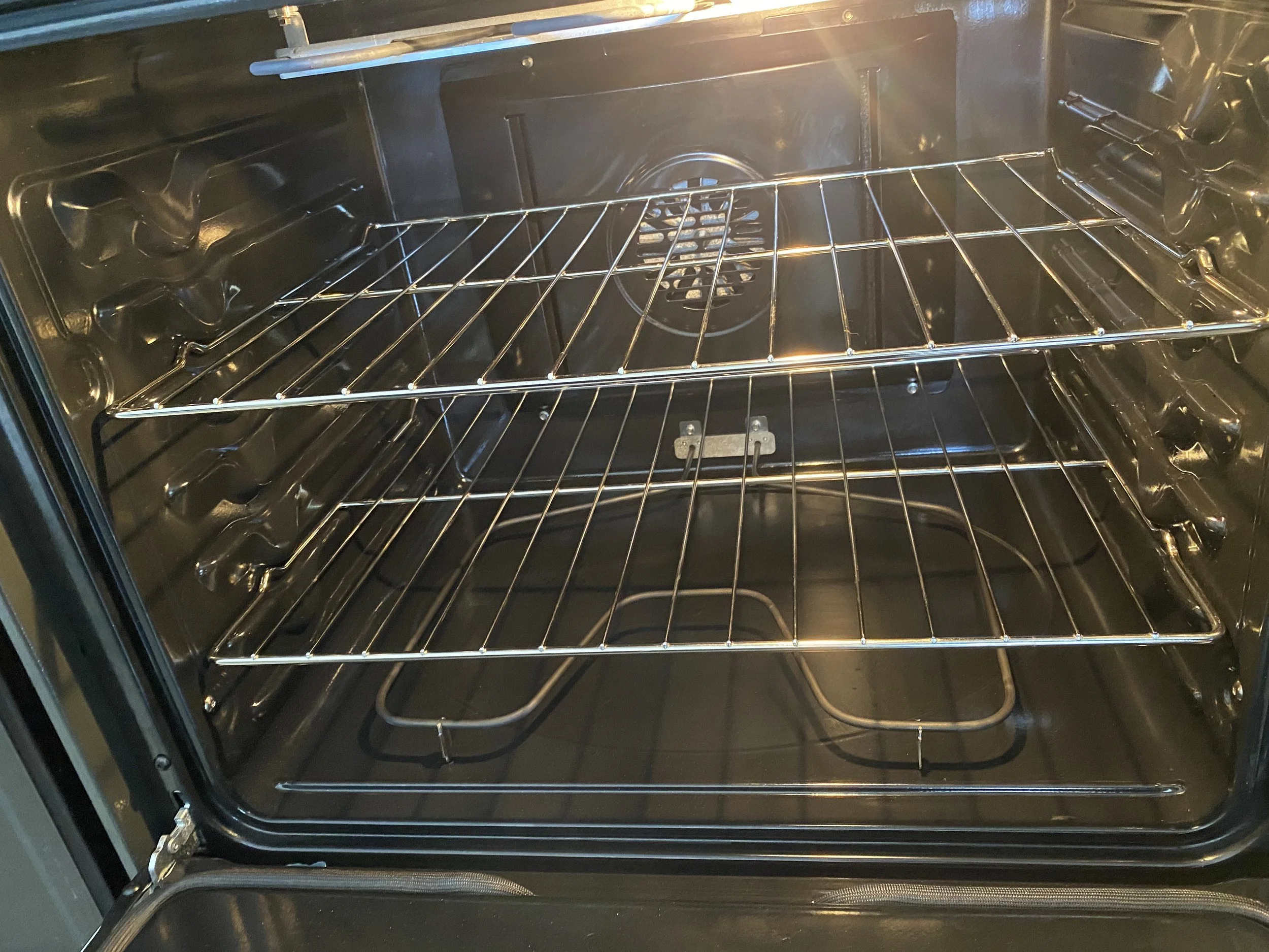Empty modern oven with oven racks, interior light on.