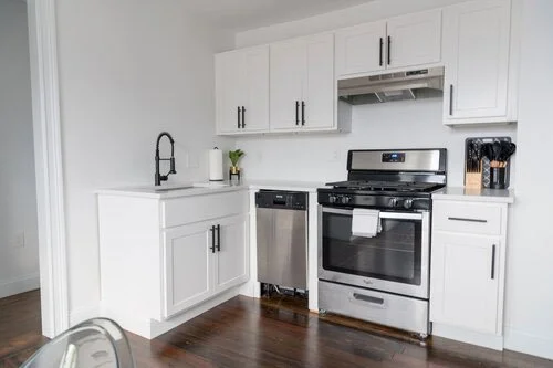 Airbnb bedroom after professional cleaning,Modern kitchen with white cabinets, stainless steel oven, dishwasher, black faucet, and wooden floor.