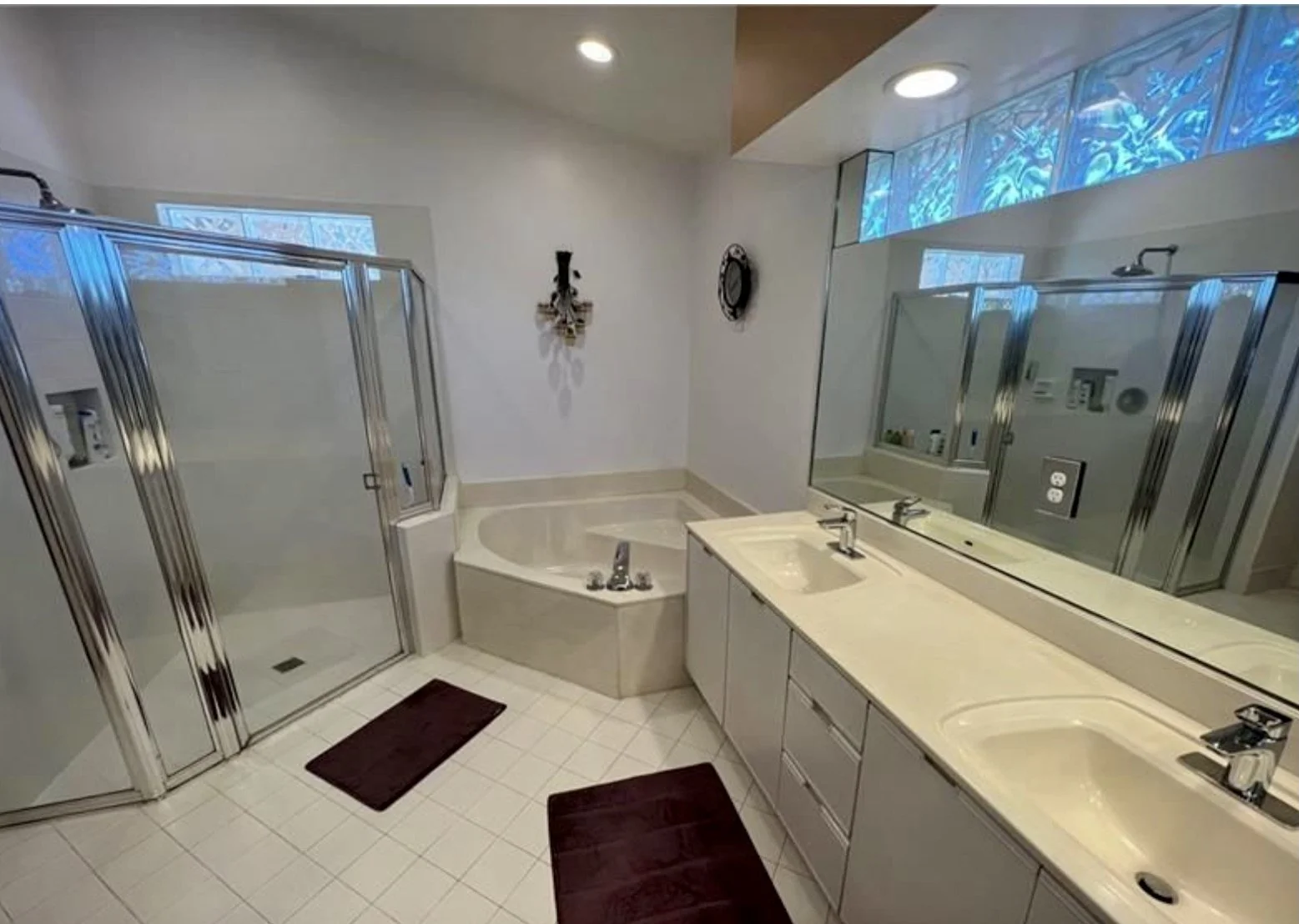 Bathroom featuring a shower with glass door, a bathtub, a double sink vanity with large mirror, a window with blue art, and decorative wall-mounted art pieces.