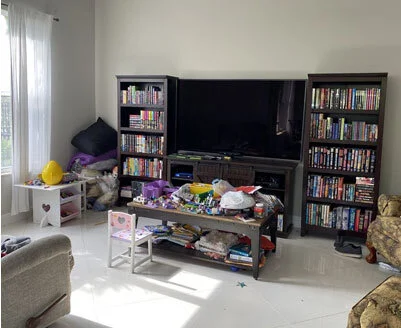 Residential house cleaning in Fort Lauderdale ,Living room with TV, bookcases, and a table cluttered with toys and clothes