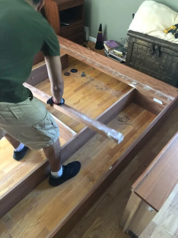 Professional moving  in  South Florida move,Person assembling a wooden bed frame in a bedroom, with some coins, books, and a cone on a nightstand in the background.