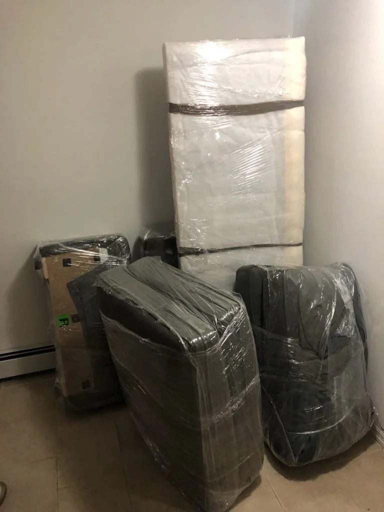 Professional moving truck for a South Florida move,Four large items wrapped in plastic in a corner of a room, including two suitcases, a box, and a large rectangular package leaning against the wall.