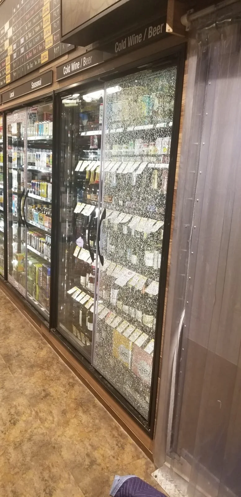 General Labor Service Refrigerator with a broken, spray-painted glass door filled with bottles, and a supermarket aisle in the background.