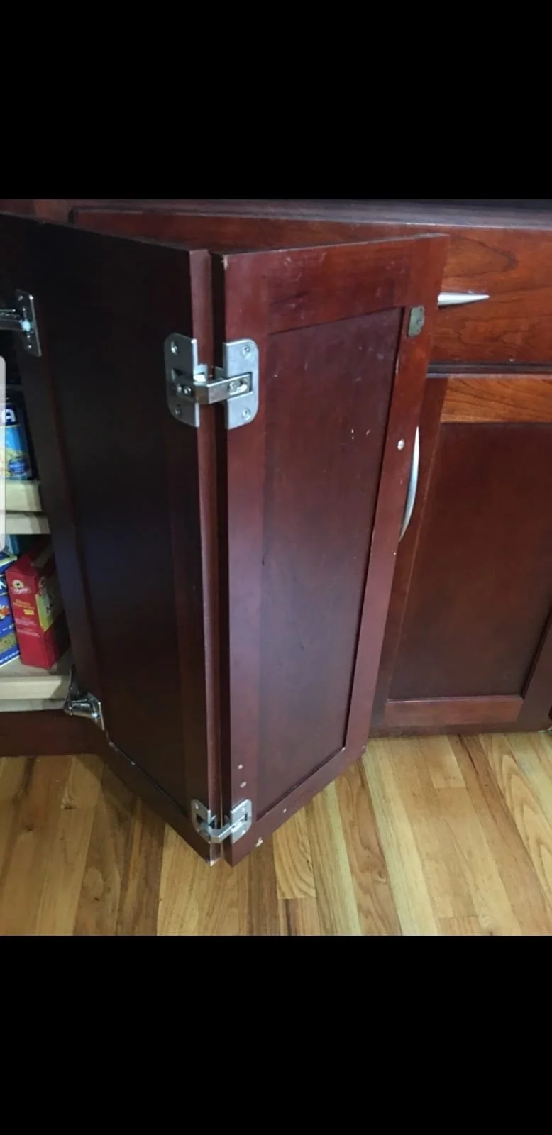 Post-construction cleaning team in Broward County,A dark wooden kitchen cabinet door partially open, showing hinges and part of an interior shelf with canned goods, on a wooden floor.