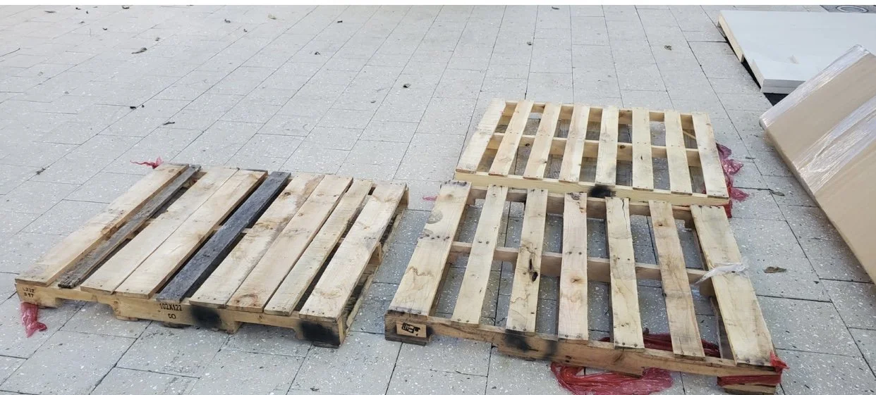 PicK Up and Delivery, Two wooden pallets on the floor, one on top of the other, with some red debris underneath, in an indoor setting.