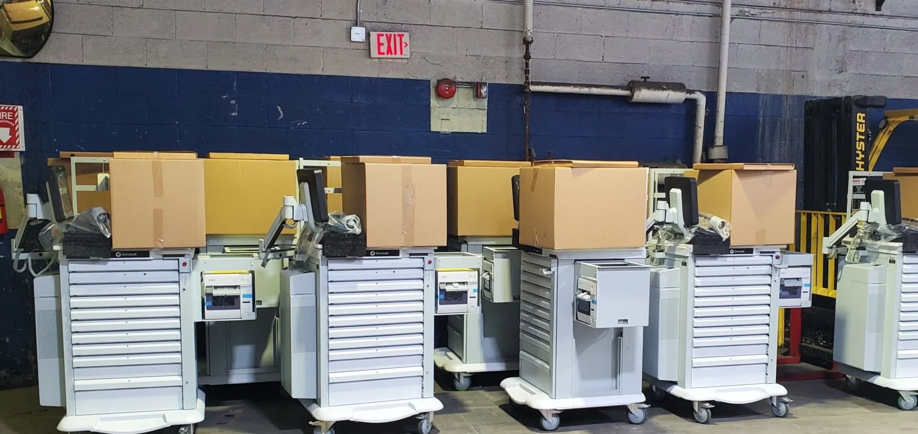  professional unloading service, Multiple medical imaging machines lined up in a storage area, with cardboard boxes placed on top of them.