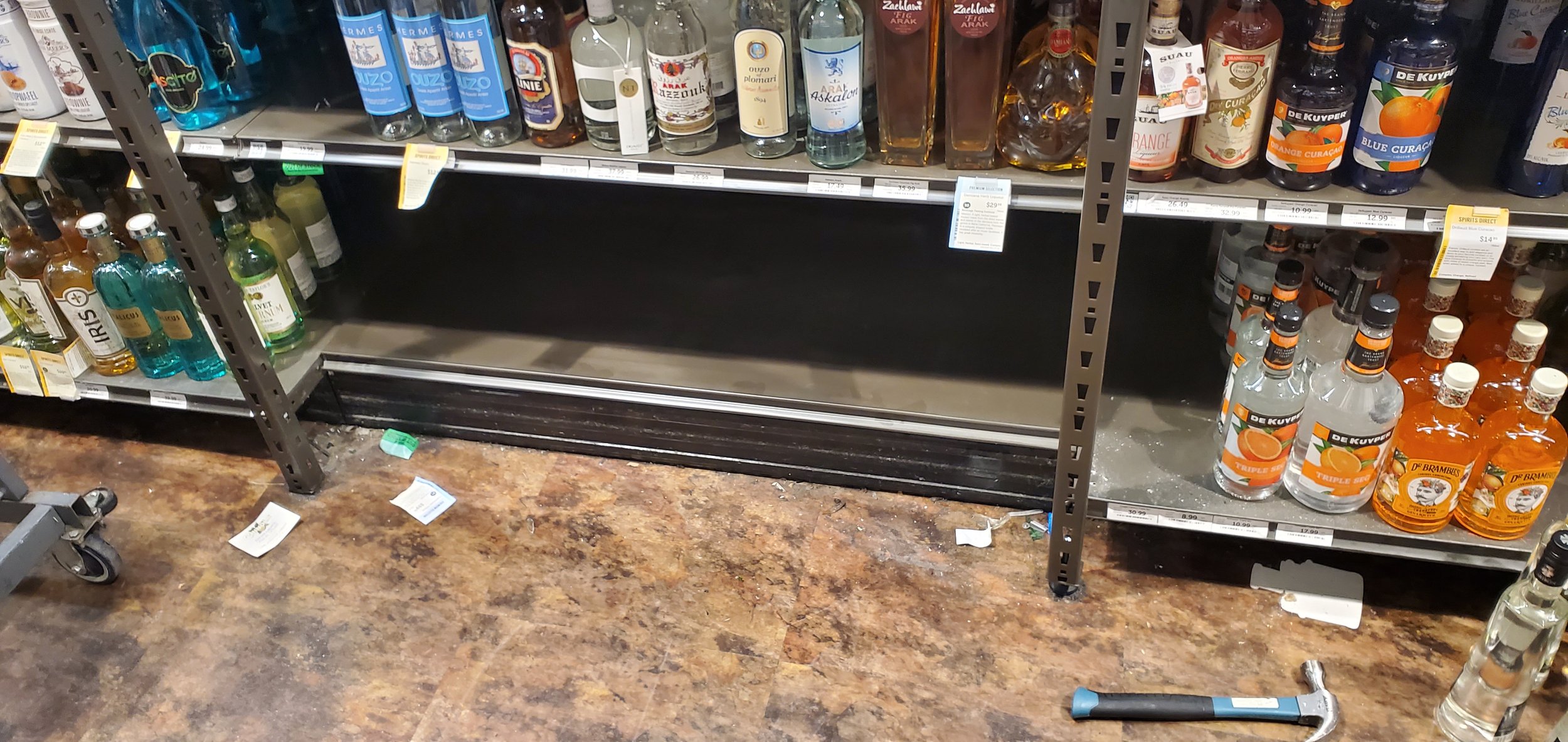 commercial Handymen Service,Empty store aisle shelf with liquor bottles and beer bottles on metal racks, scattered trash and a hammer on the floor.